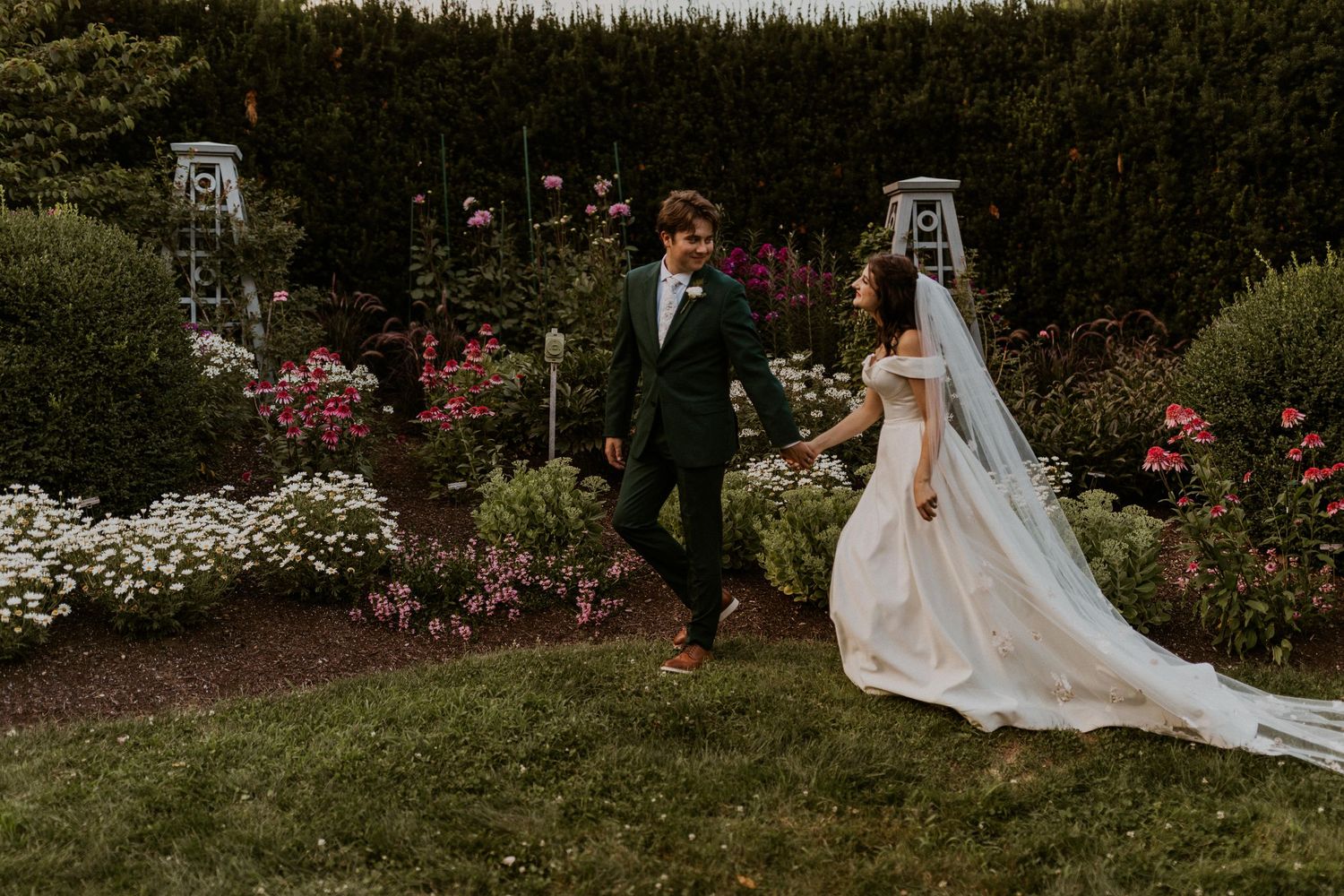 Wedding couple walking through a lush garden with blooming flowers and greenery.