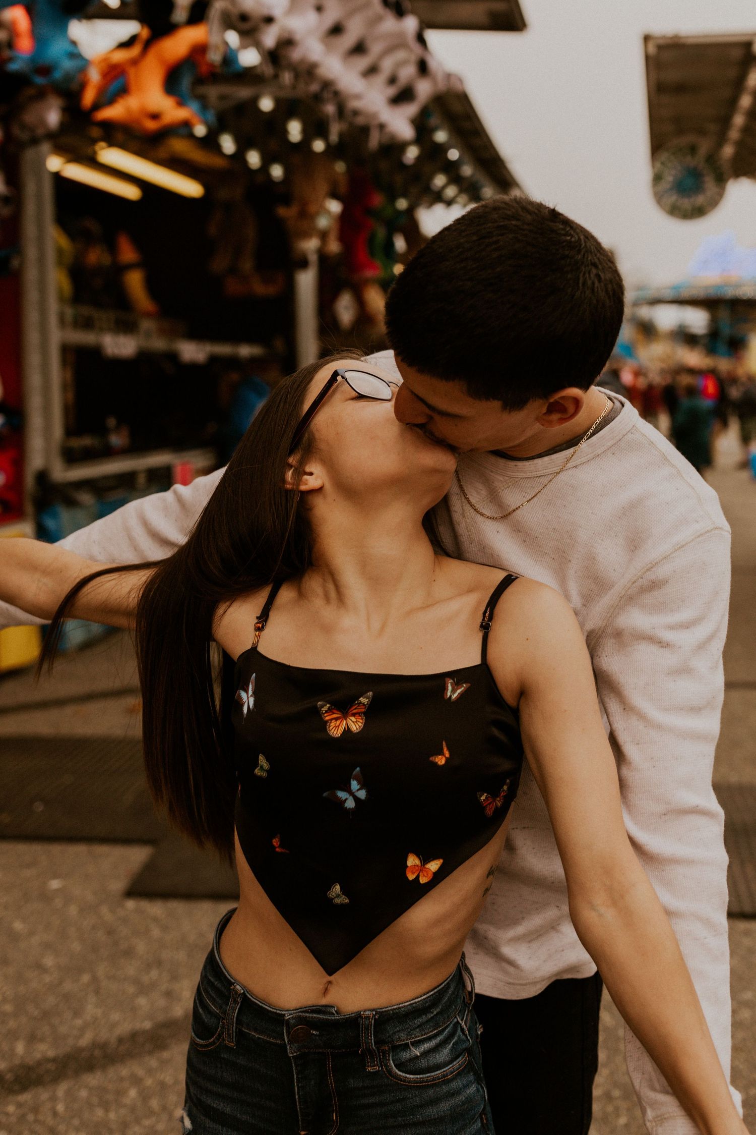 Romantic couple in casual attire sharing intimate moments at a carnival with butterfly details on her top.