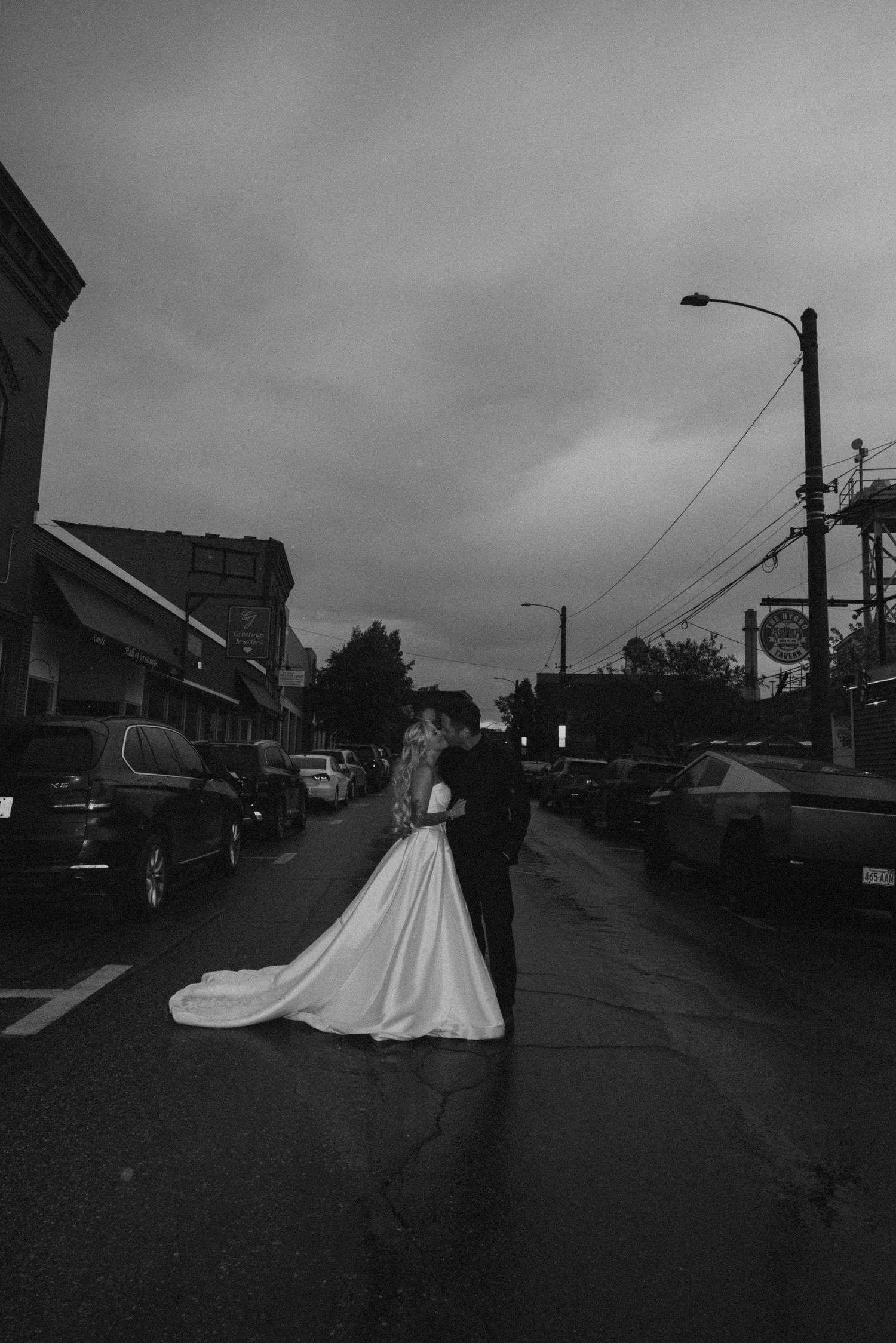 Bride and groom kissing in middle of street at dusk in dramatic black and white photo.