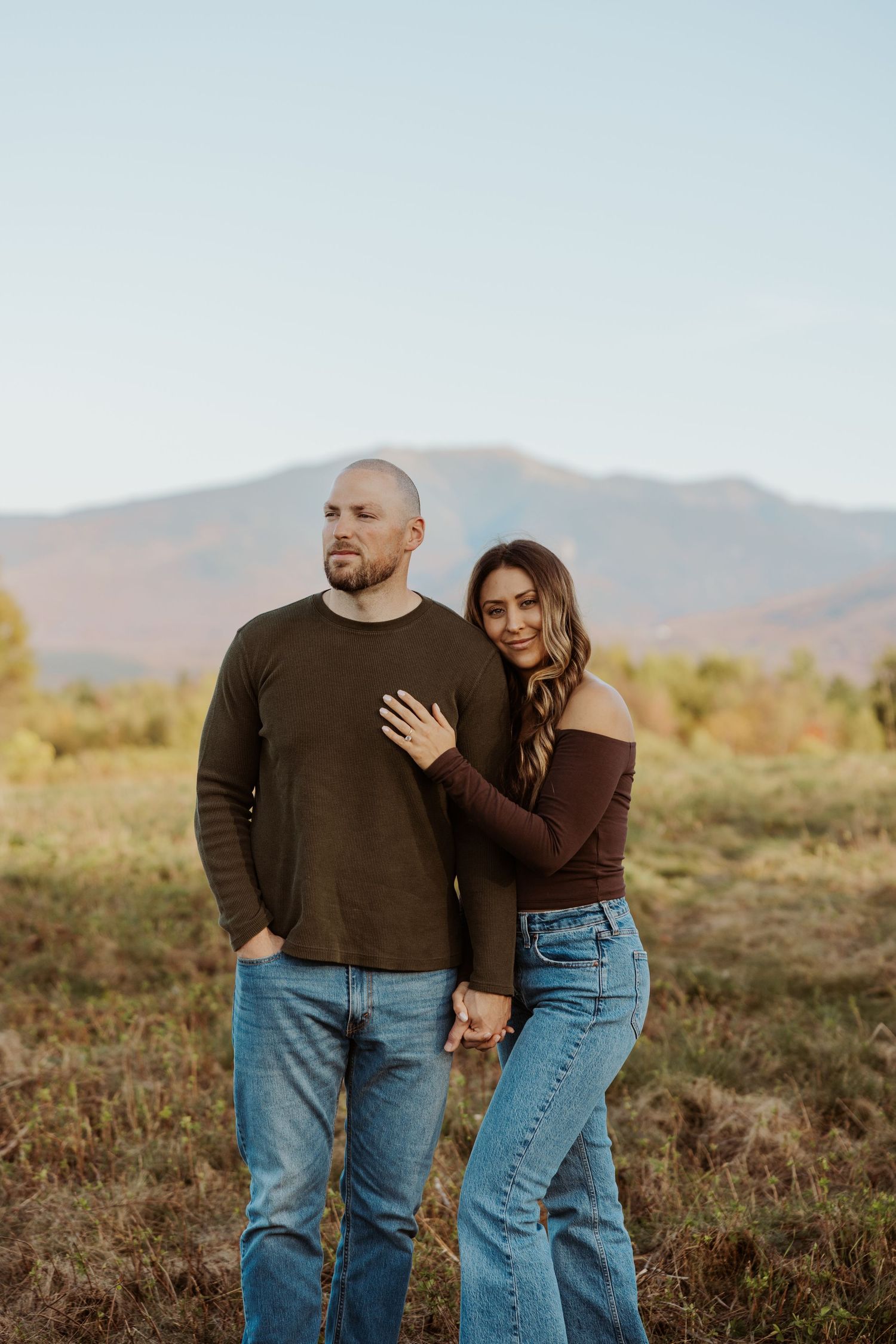 Couple posing together in a field with a scenic mountain backdrop at dusk.
