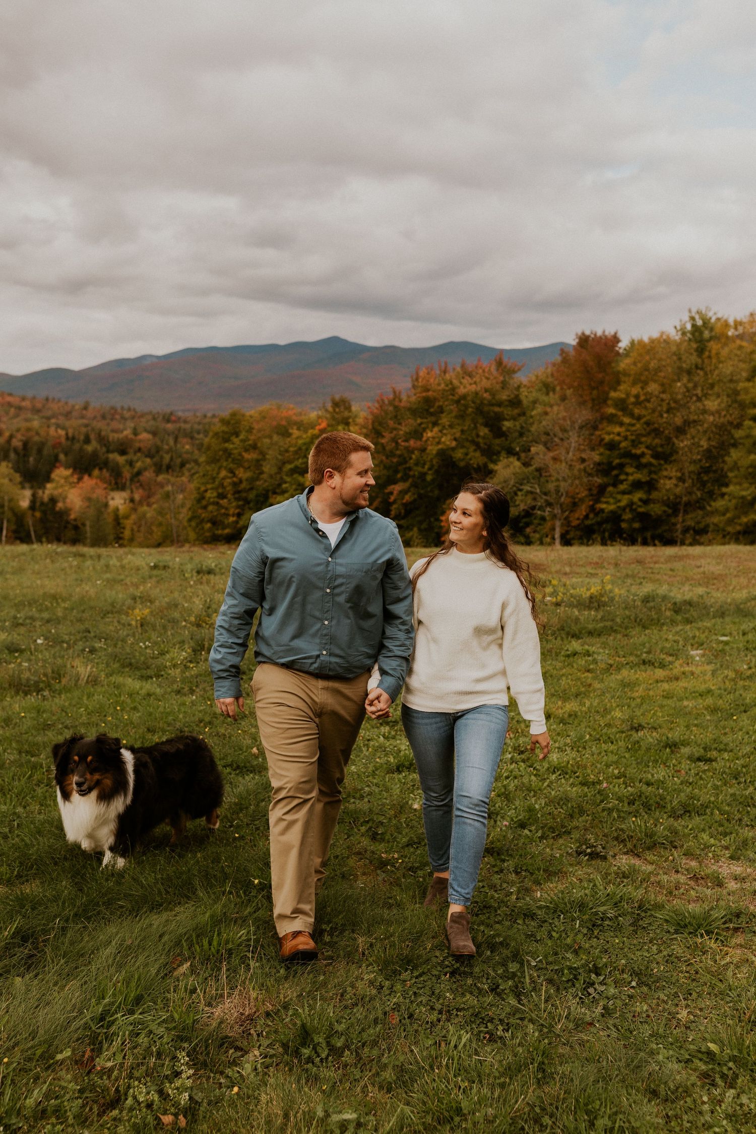 Paige and Michael walking through the field with their dogs during their engagement photoshoot in the white mountains.