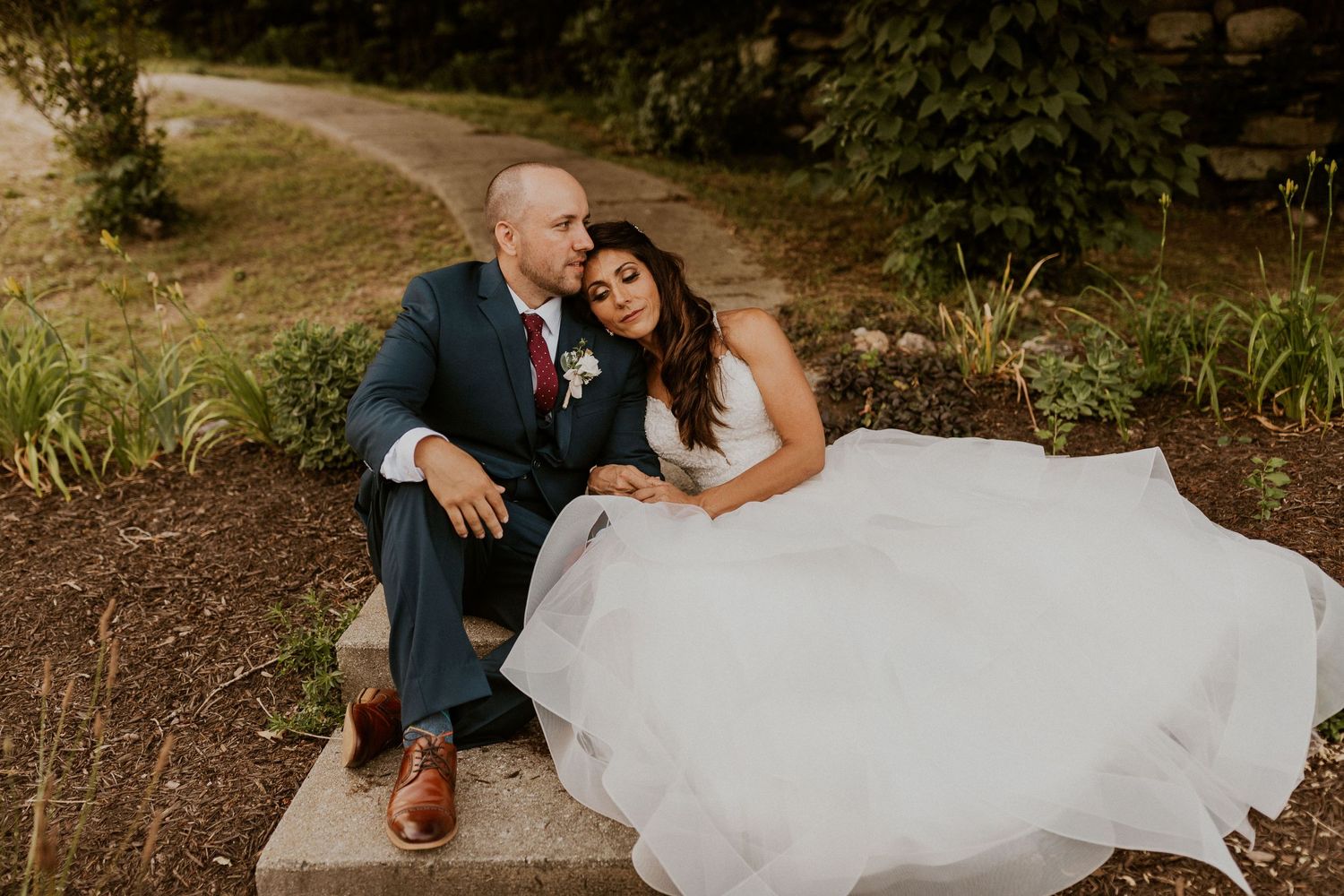 Couple in wedding attire walks through a lush green hillside setting on their special day.