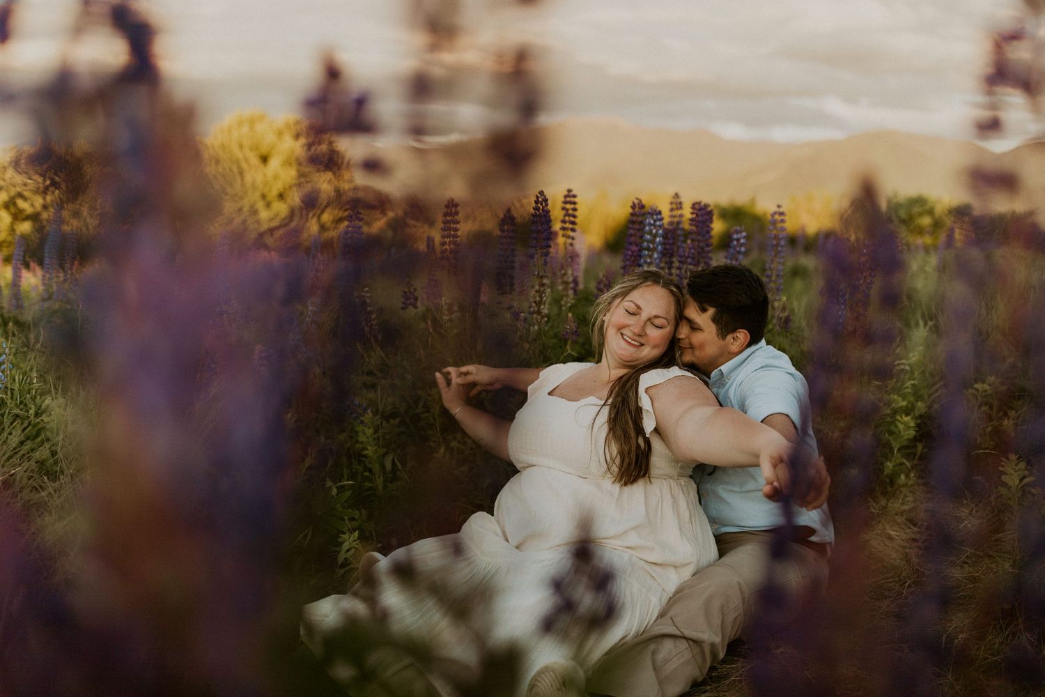 Terise and Jose cuddling up together in a field of purple lupines in Sugar Hill New Hampshire.
