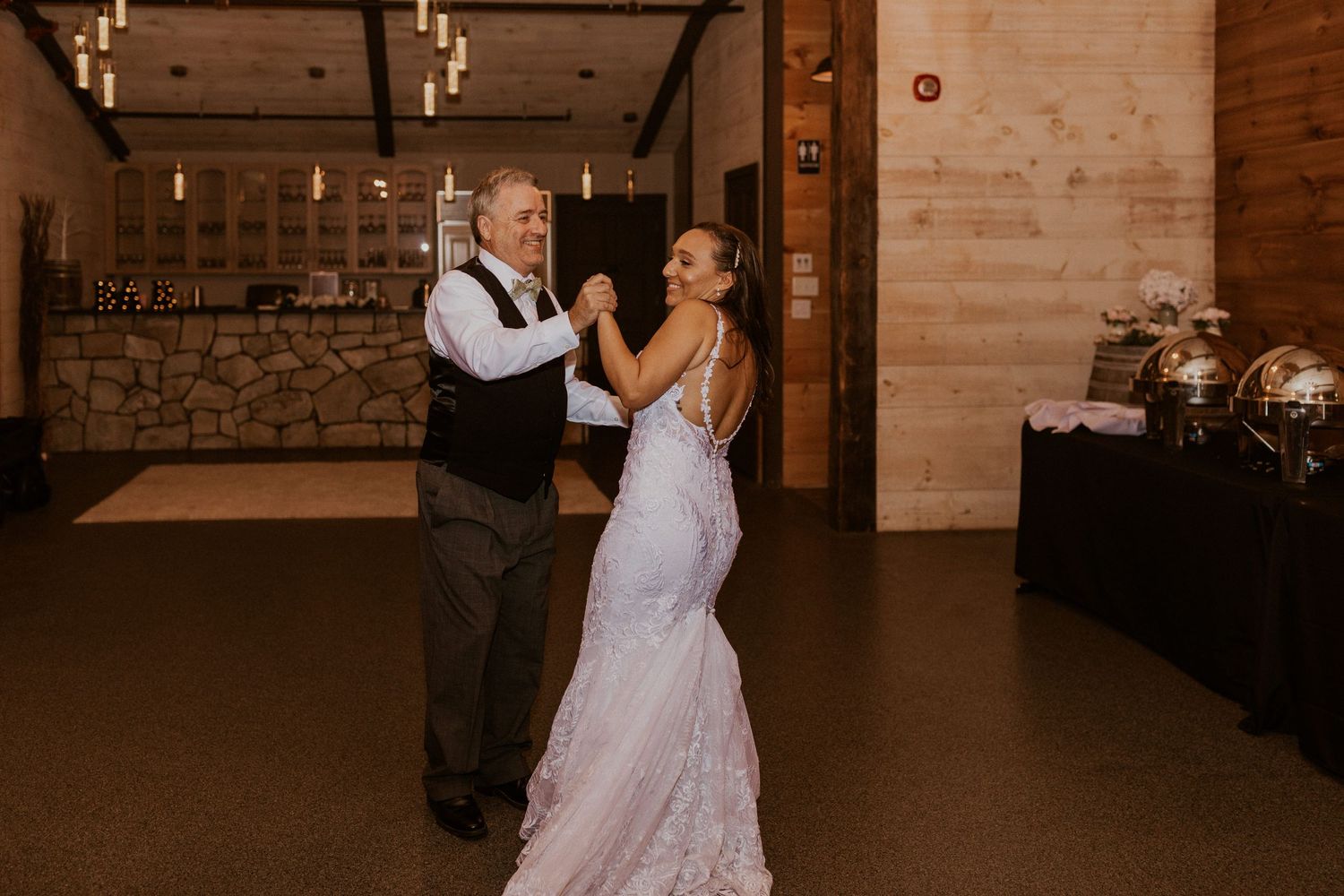 Couples dancing at a rustic barn wedding reception with warm ambient lighting.