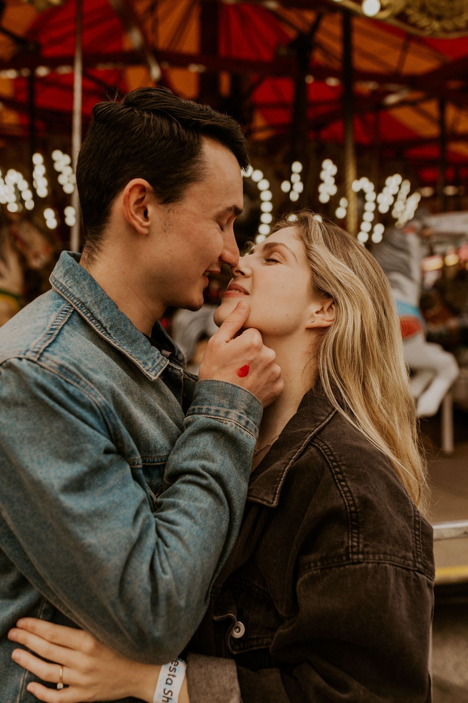 Romantic couple sharing an intimate moment at a carnival with twinkling lights in the background.
