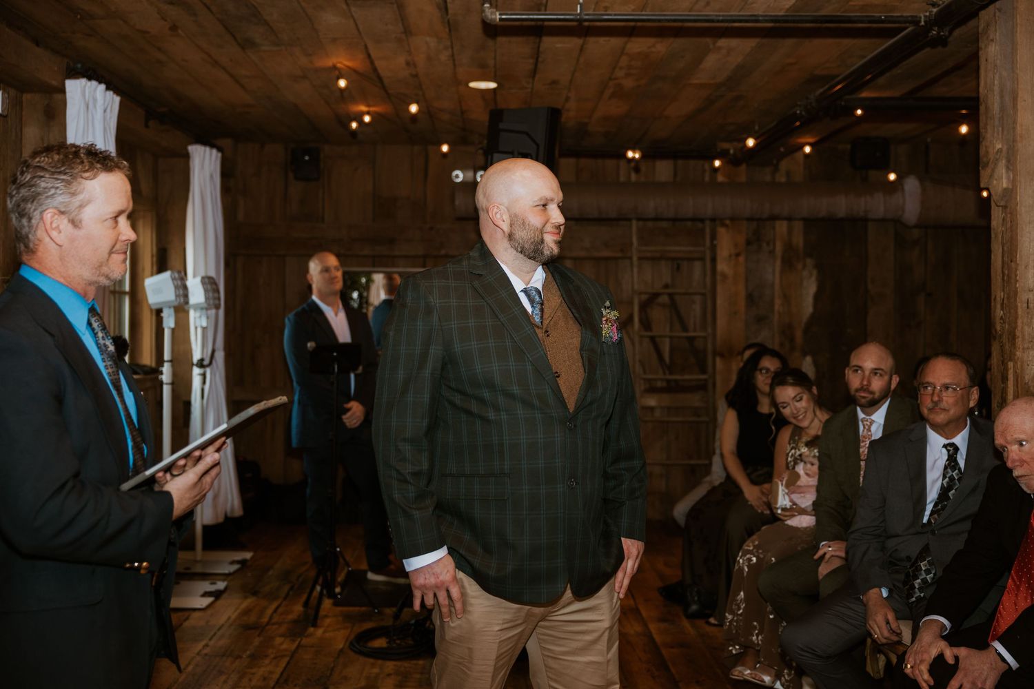 People gather in a rustic barn venue for a social event with exposed wooden beams and warm lighting.