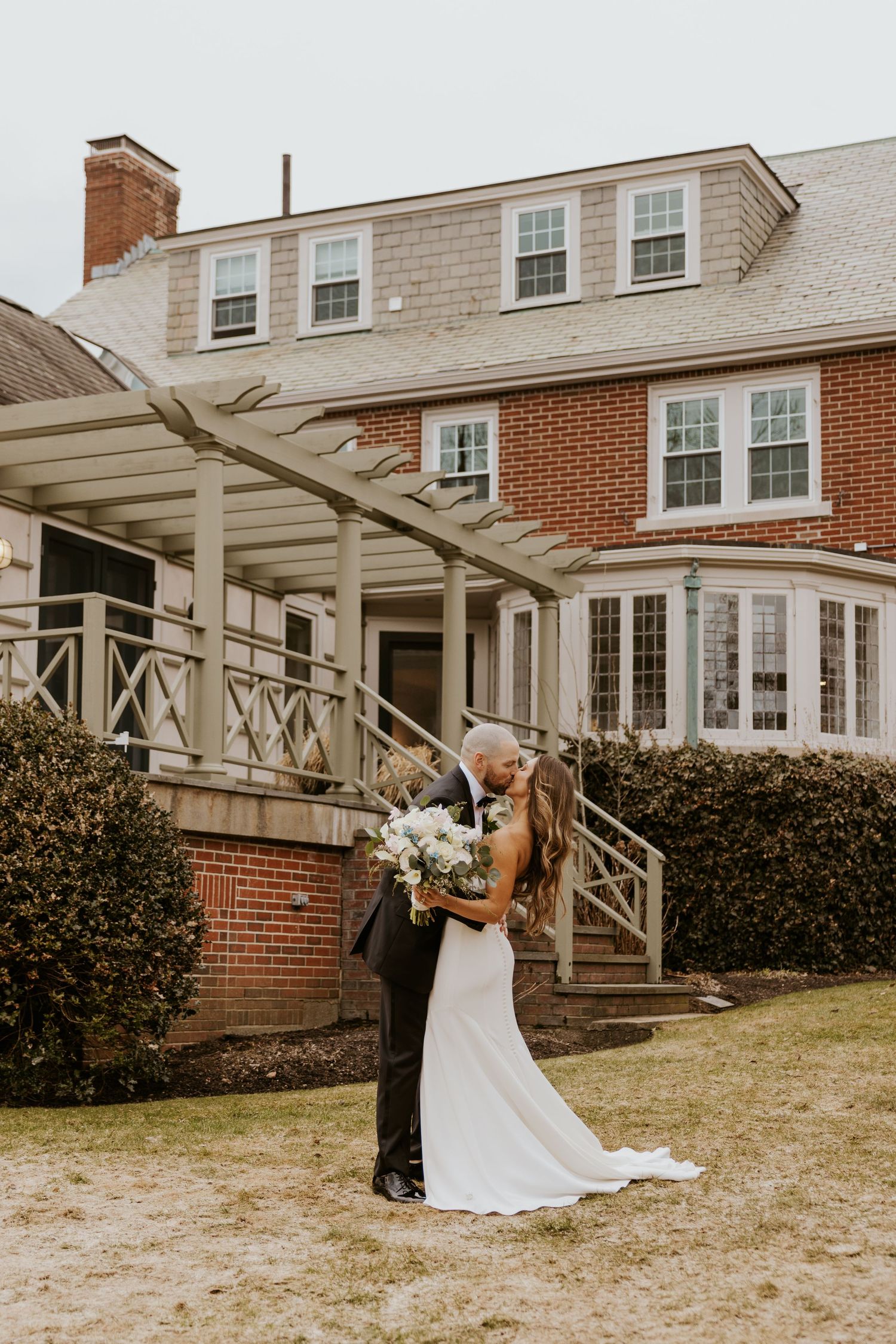 A romantic wedding couple shares intimate moments outside a brick colonial style house with a white pergola.