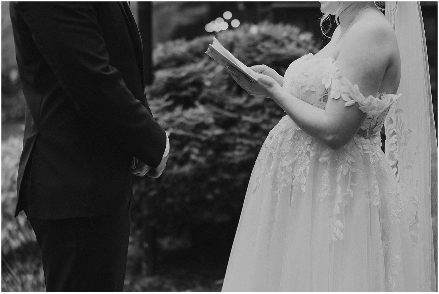 Black and white close-up of wedding ceremony with bride reading vows.