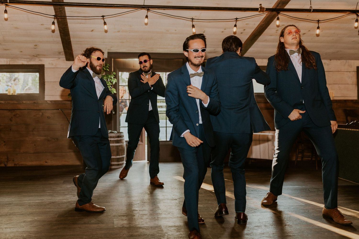 Wedding guests dancing and celebrating on a wooden dance floor under string lights.