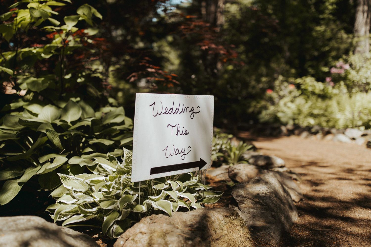 Decorative wedding signage placed along a garden path with green foliage in the background.