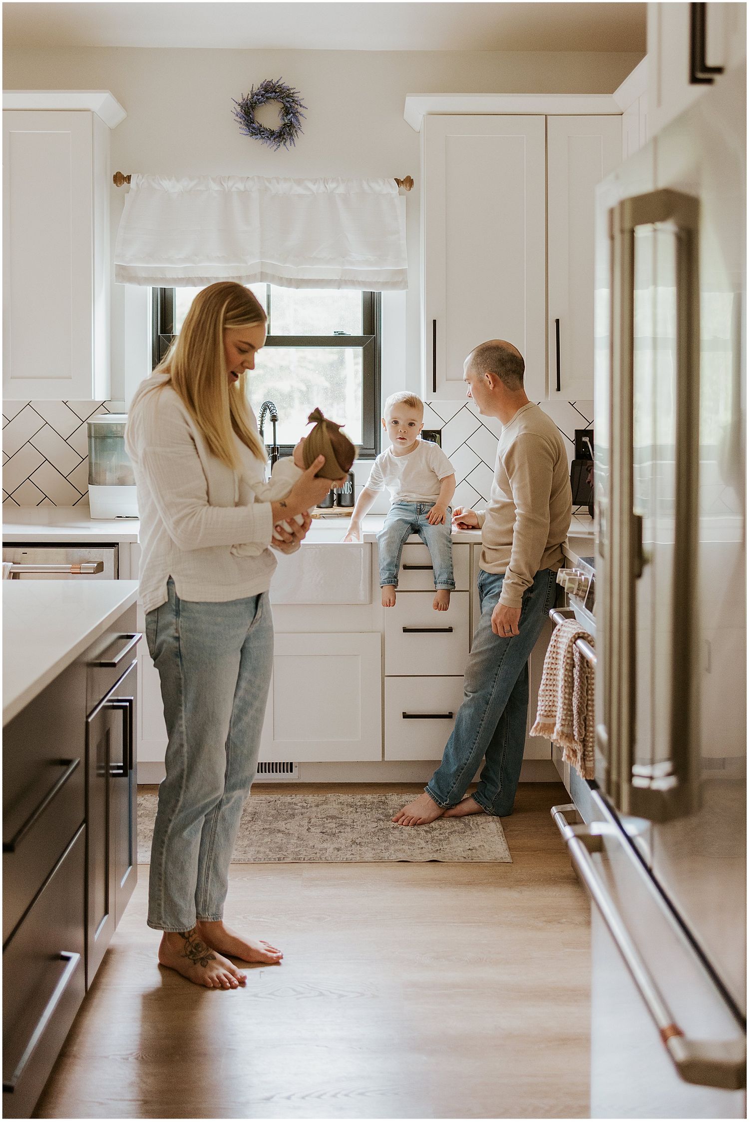 A family in their bright white kitchen in New Hampshire taking photos with their newborn baby