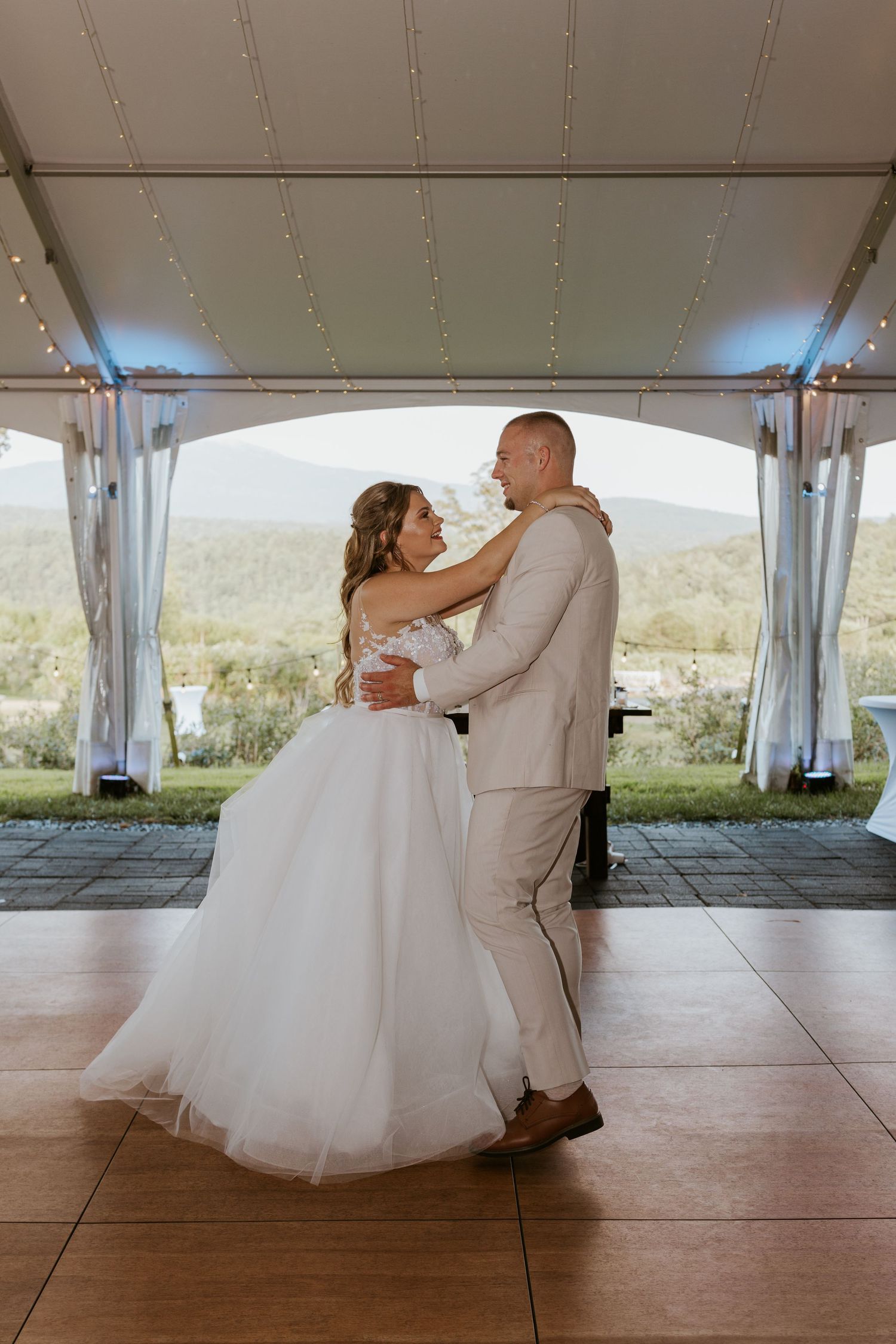 Bride and groom sharing romantic first dance under elegant tent with mountain views at dusk.