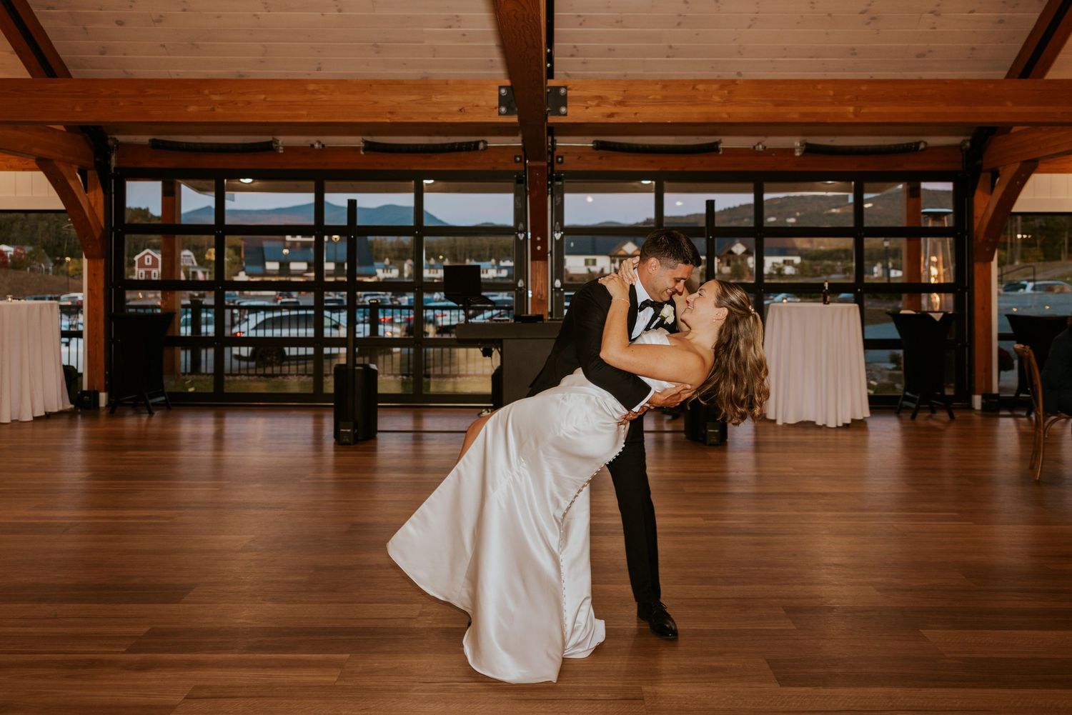 Groom dips bride in romantic first dance finale at wedding reception with scenic backdrop.