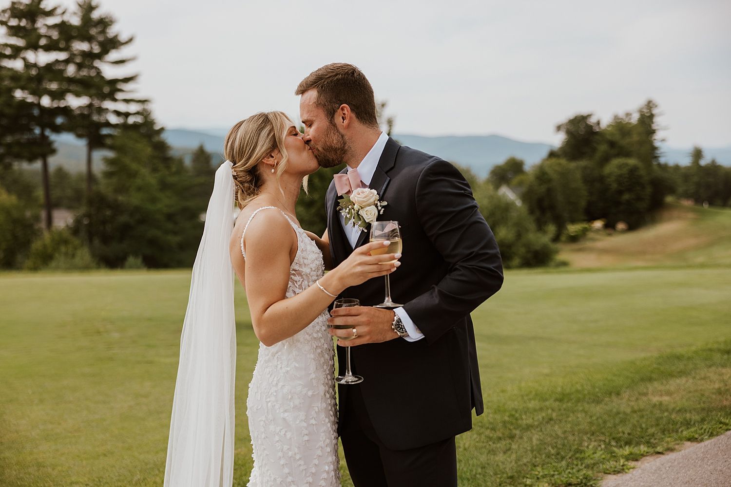 Bride and groom kissing while holding champagne at their wedding at the Sunset Pavilion at Owl's Nest Resort in New Hampshire