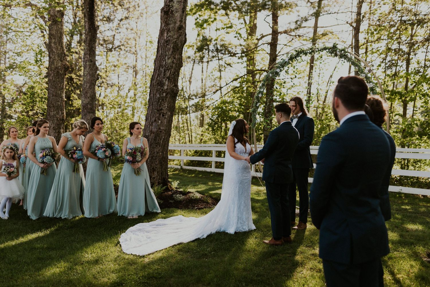 Chrissy and Mike holding hands as their wedding ceremony begins. It is a lovely spring day with the sun shining.