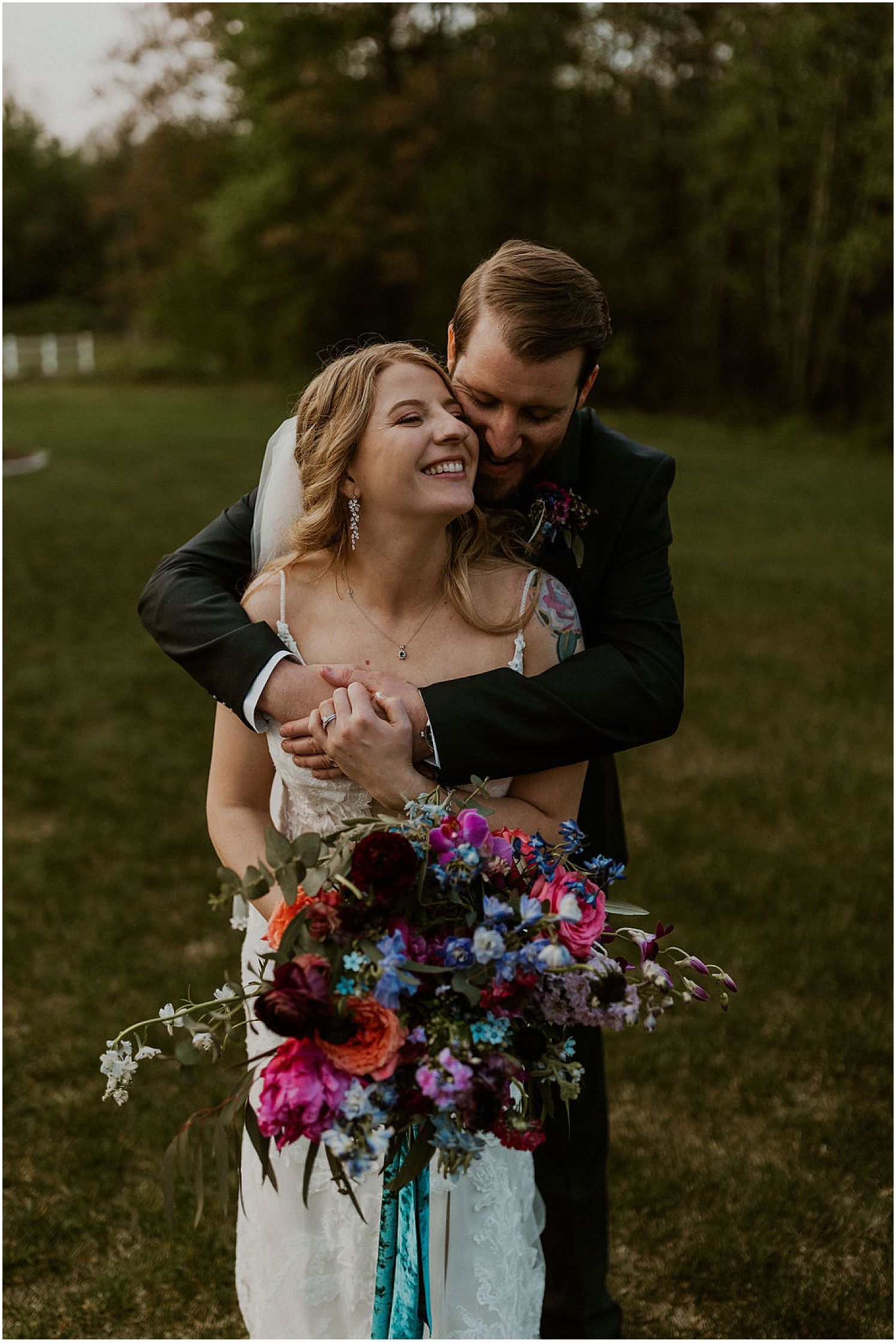 Joyful wedding moment captured with vibrant floral bouquet against green outdoor backdrop.