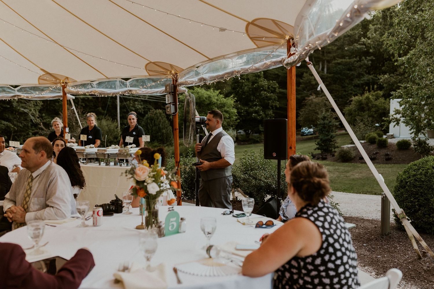 Wedding buffet setup under white tent with chafing dishes and elegant table settings.