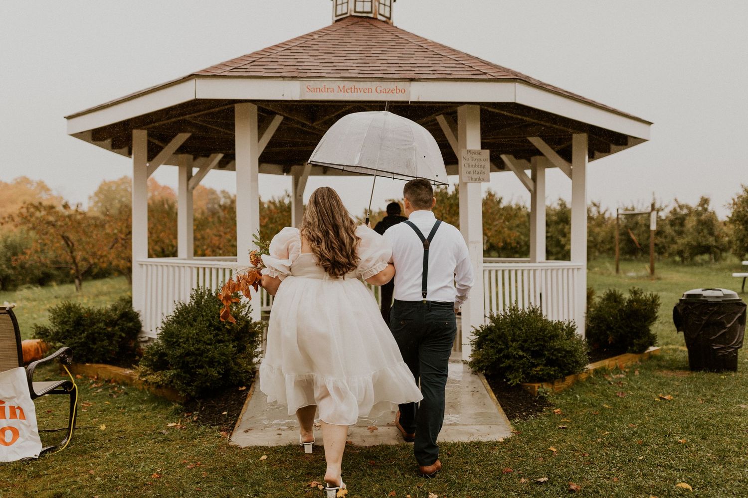 Terise and Jose entering the gazebo together under an umbrella at Carter Hill Orchard in Concord New Hampshire