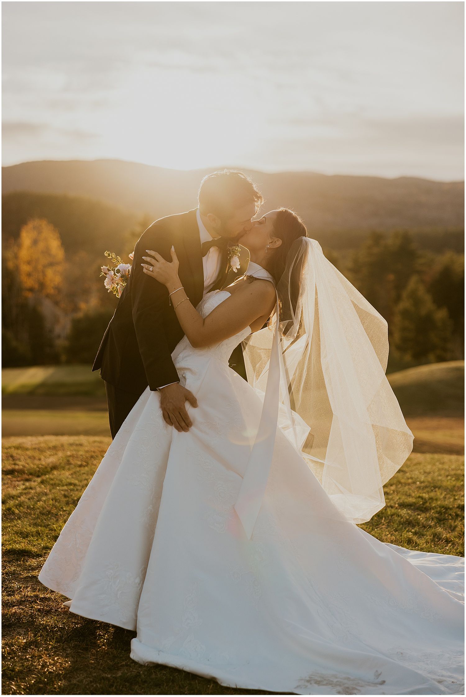 Romantic wedding couple embracing on a hilltop during sunset with flowing white dress.