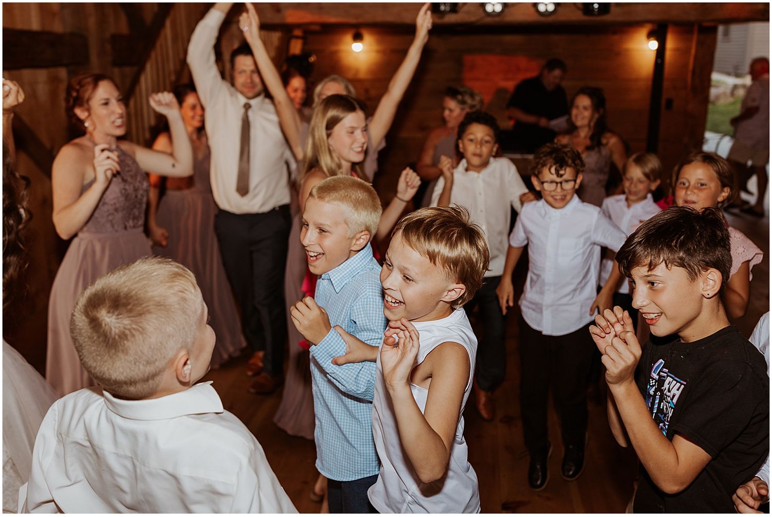 Lively celebration with guests dancing and jumping inside a wooden barn reception venue.