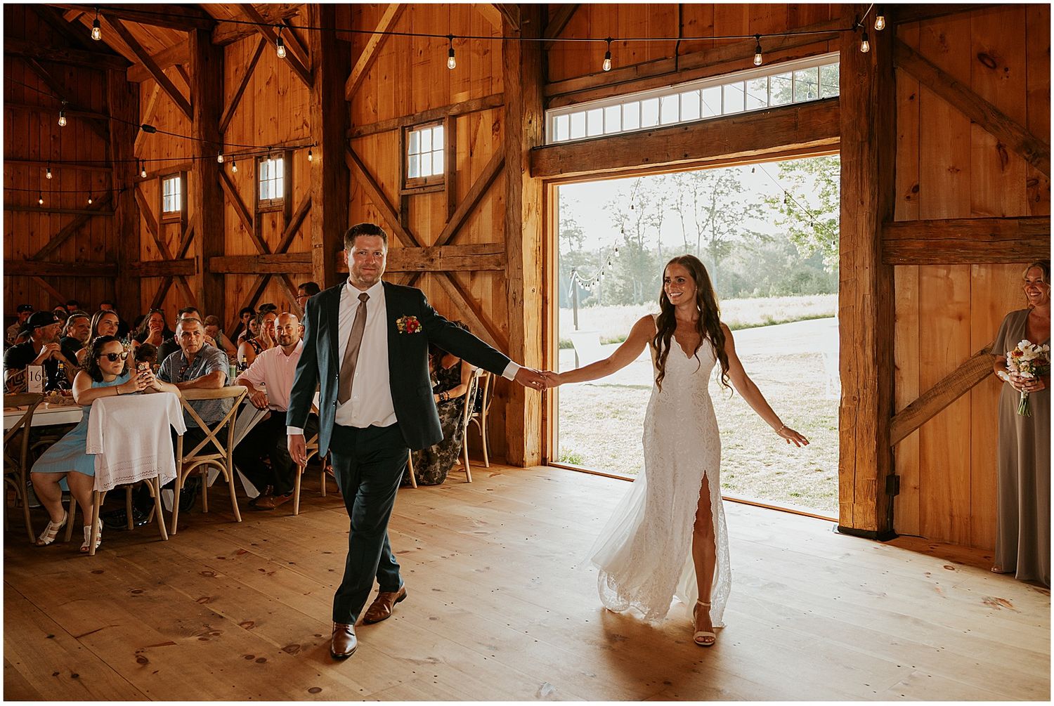Wedding party dancing and celebrating inside rustic barn venue with wooden beams.