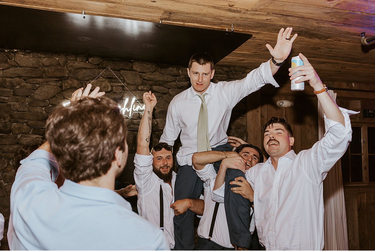 Wedding reception party with guests dancing and celebrating in a rustic indoor venue.