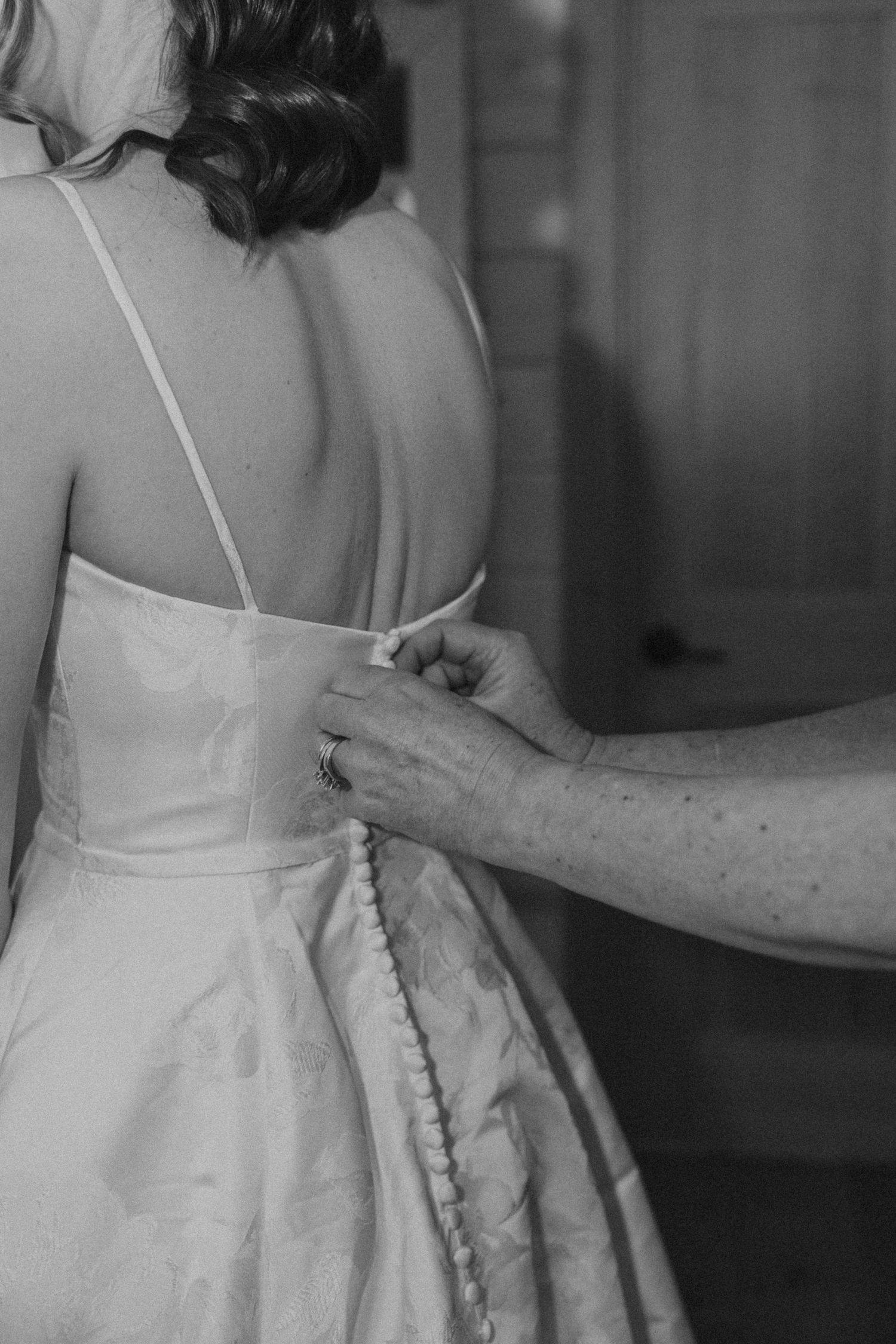 Black and white image showing the back details of a wedding dress being fastened.