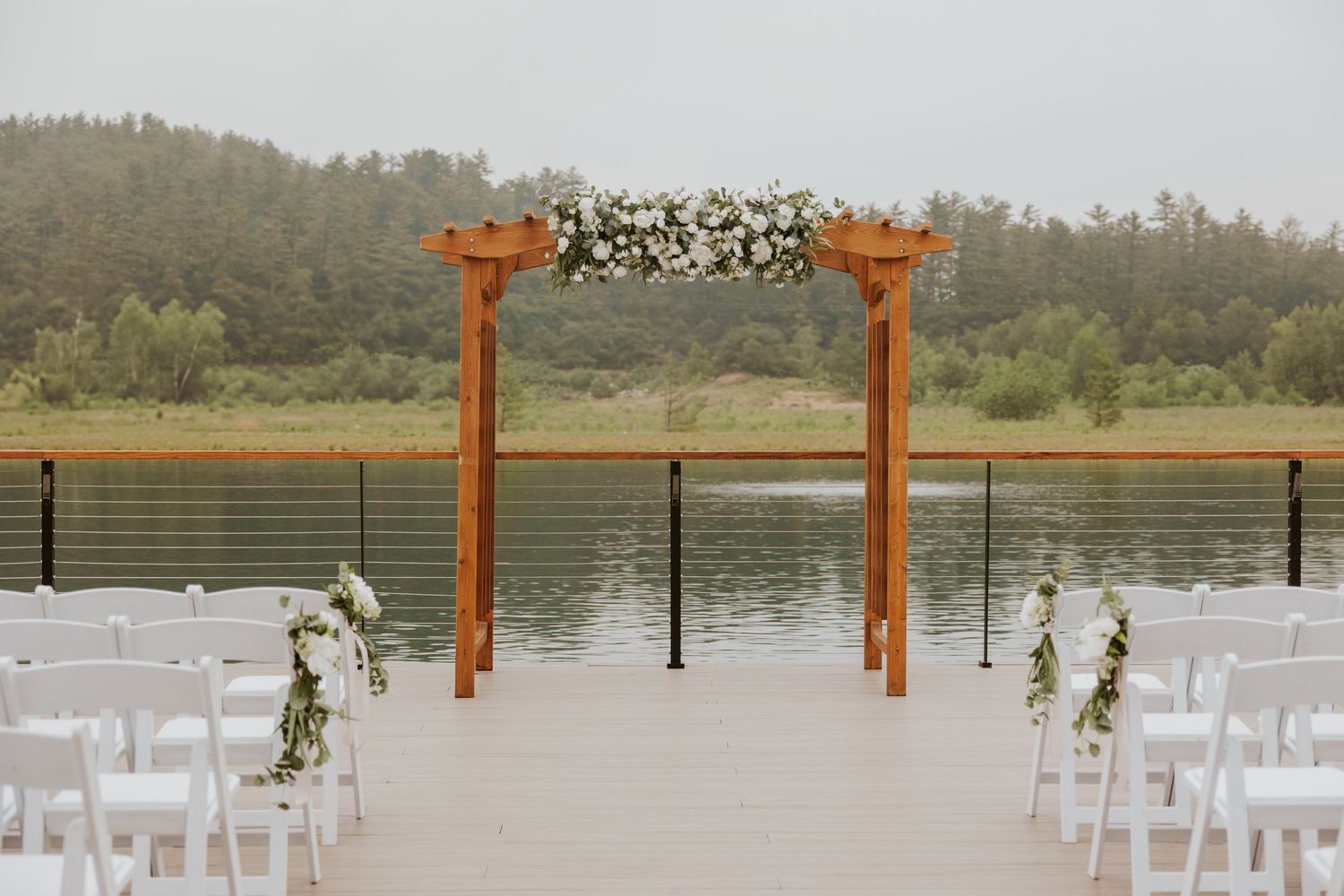 Outdoor wedding ceremony setup with wooden arch adorned with flowers overlooking a serene lake.