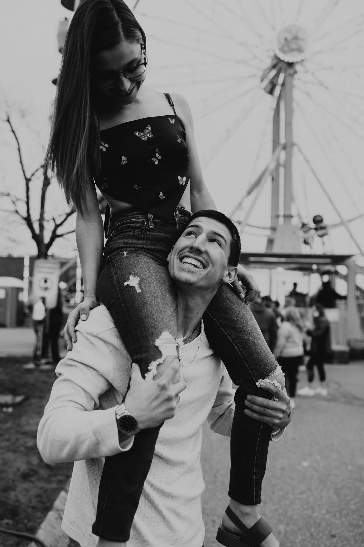 Couple sharing joyful moments at an amusement park with carnival rides visible behind them.