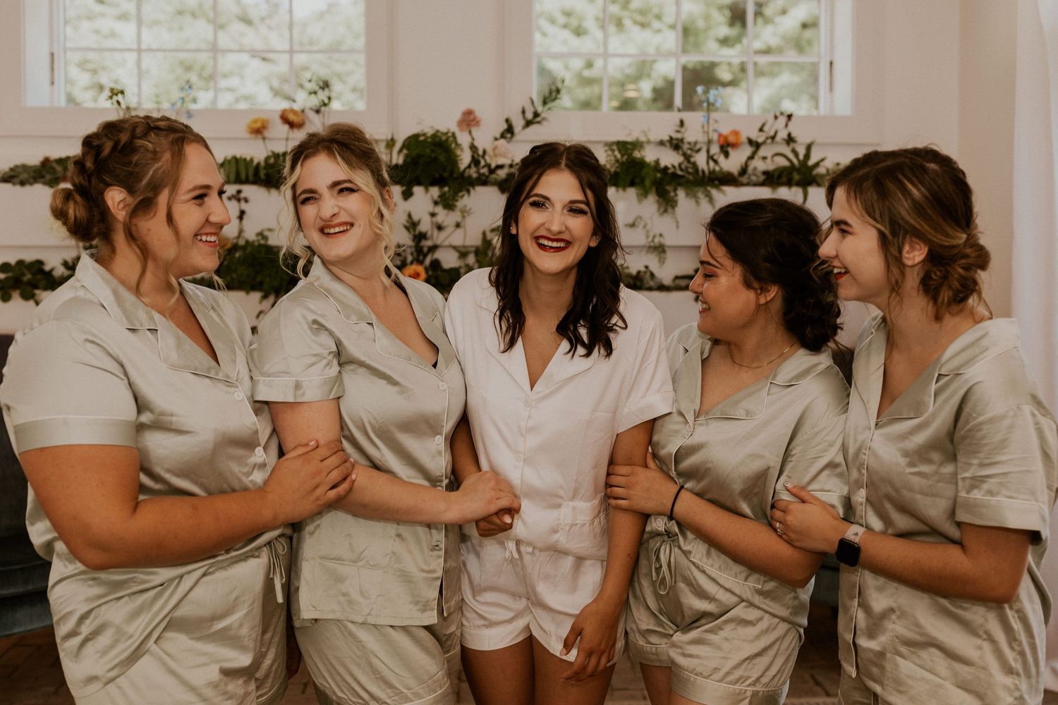 Bridesmaids in matching light colored outfits sharing joyful moments together.