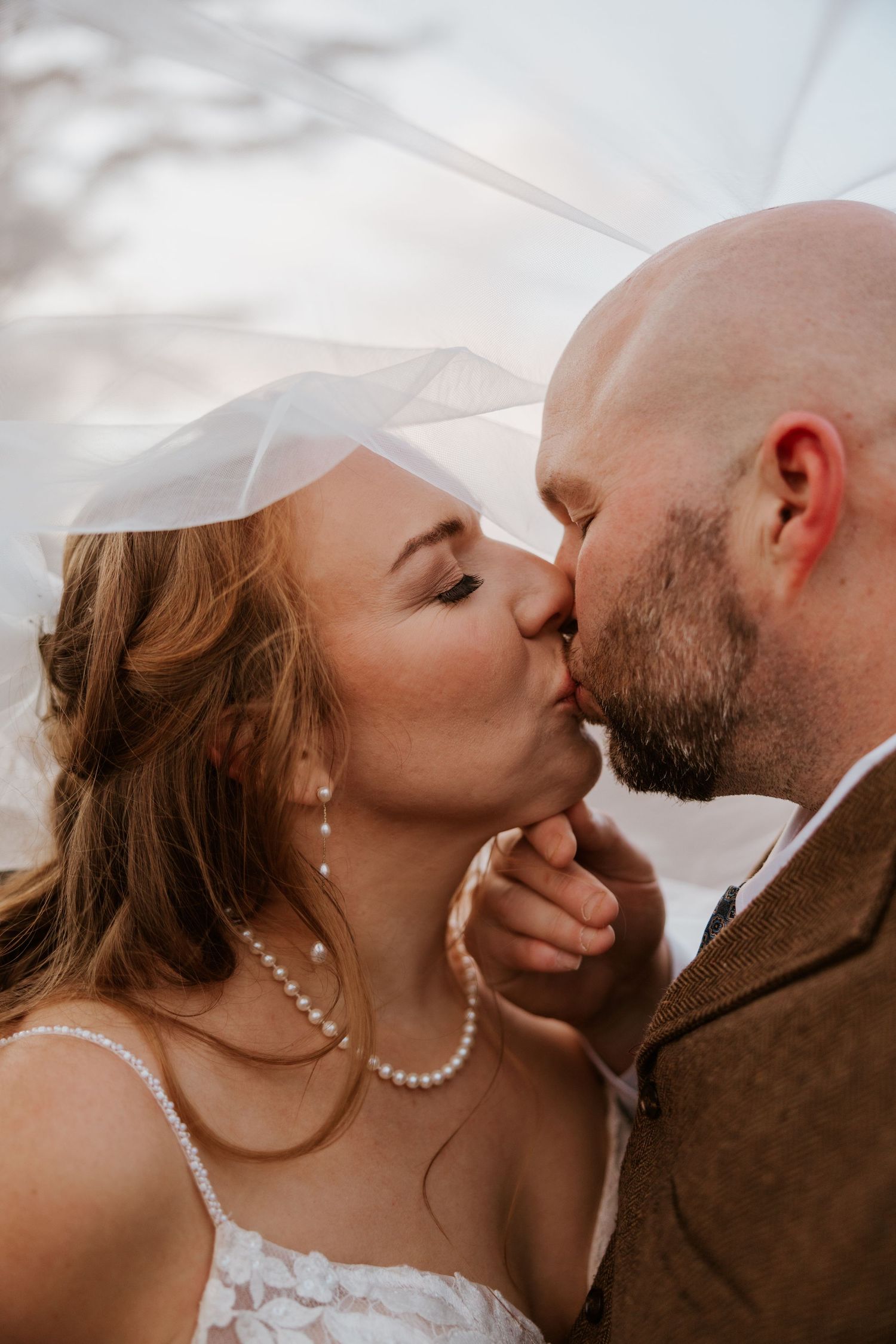 Close-up romantic wedding photos of a couple sharing intimate kisses against a bright background.