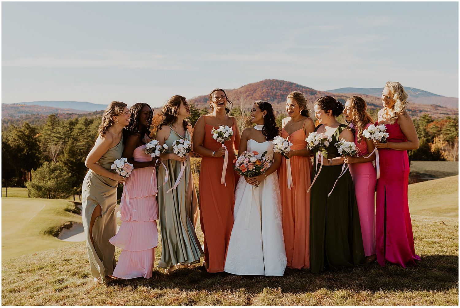 Wedding party members stand together on a hilltop against a scenic mountain backdrop at golden hour.