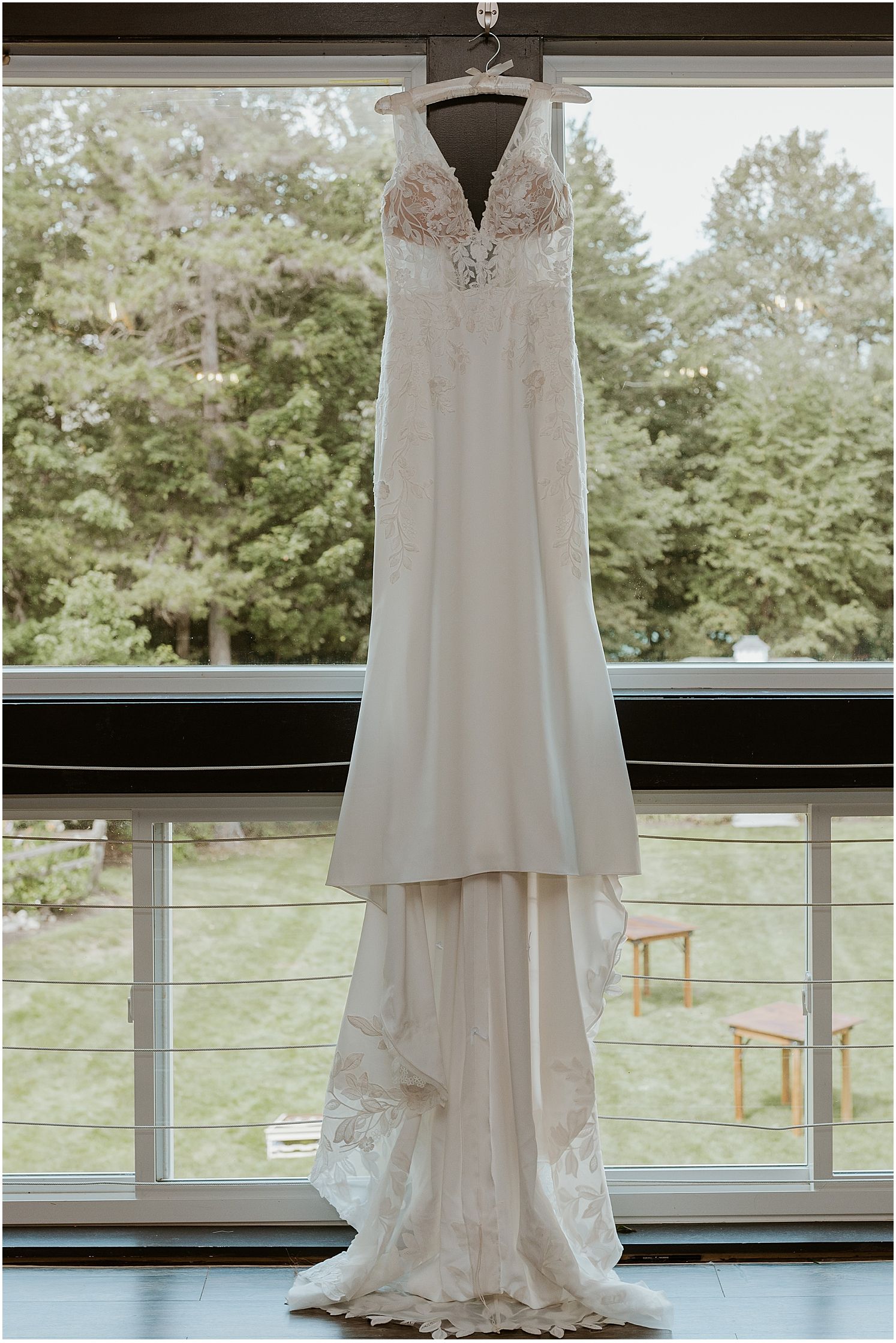 Elegant white wedding dress with lace details displayed against large windows with nature view.