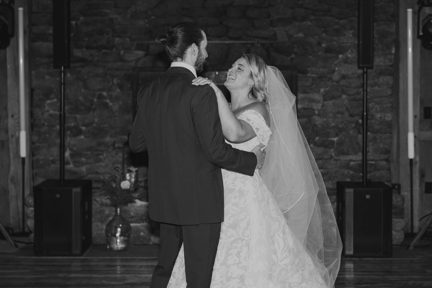 Black and white photo of bride and groom sharing their first dance in a rustic reception venue.