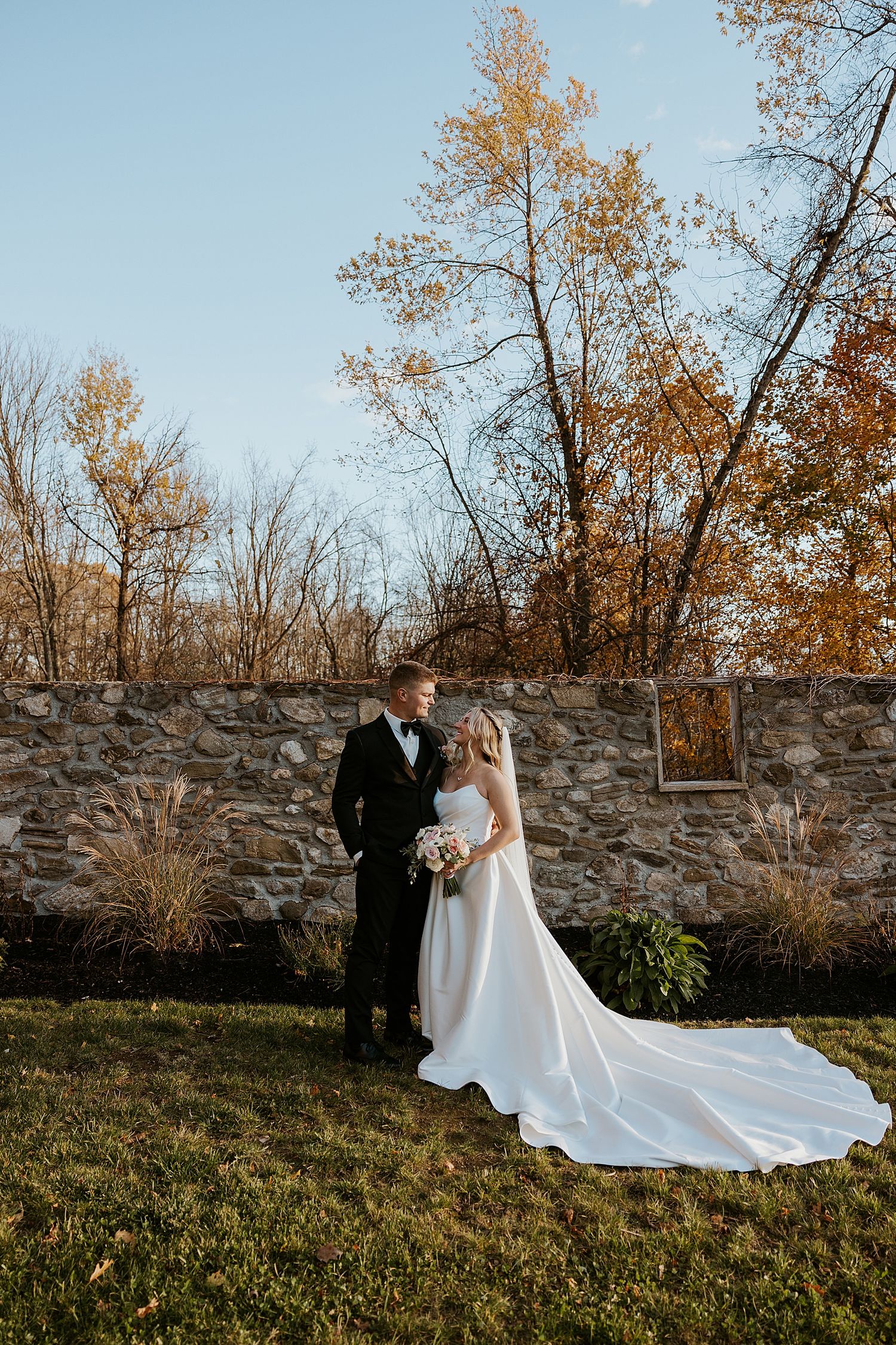 Bride and groom taking portrait photos by the stone wall at Hyla Brook Estate in NH