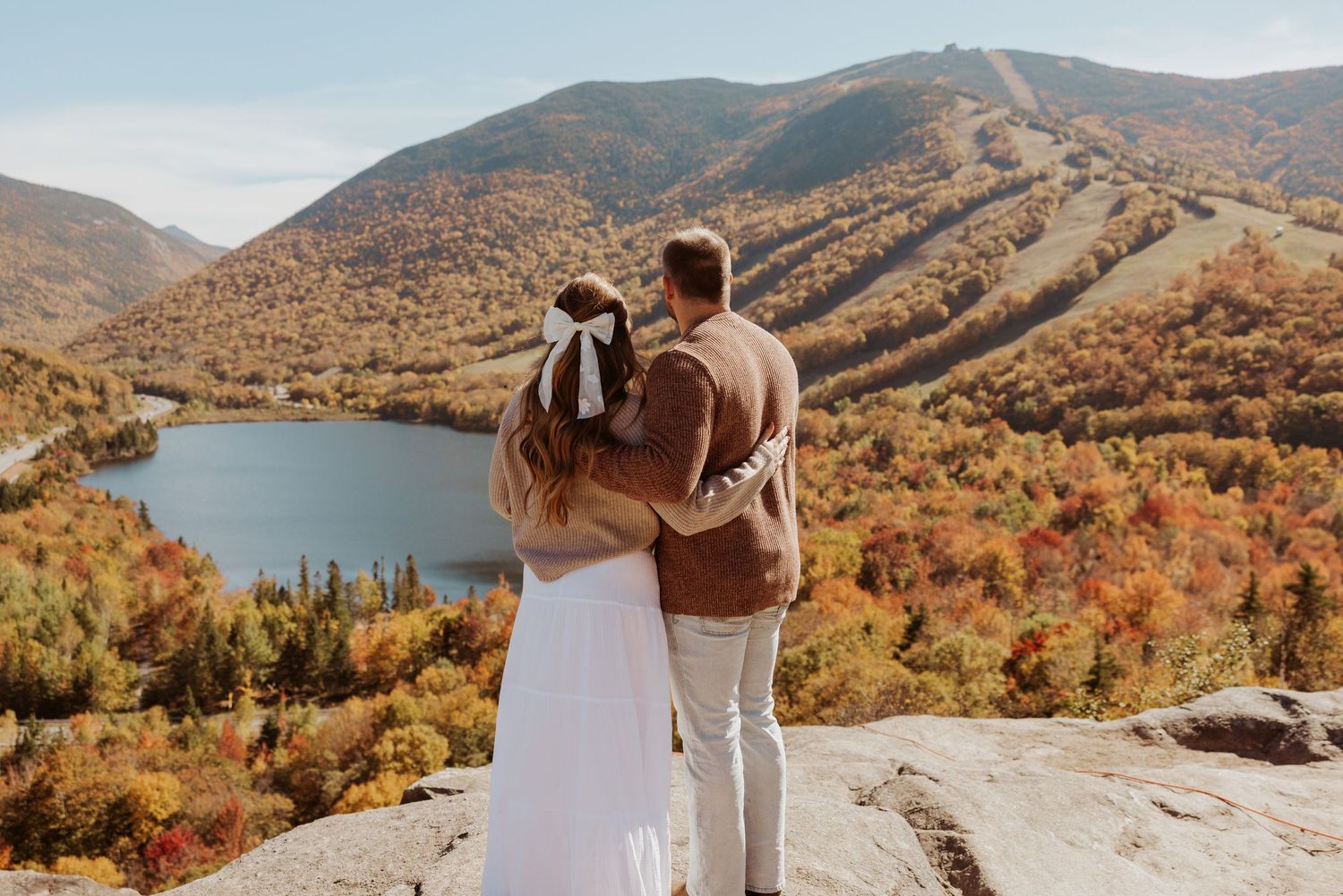 Couple standing arm-in-arm gazing at breathtaking autumn mountain and lake panoramic landscape.