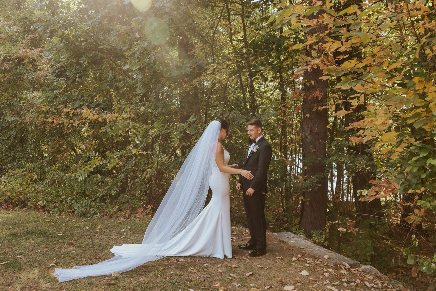 Bride and groom holding hands facing each other in a romantic autumn woodland setting.