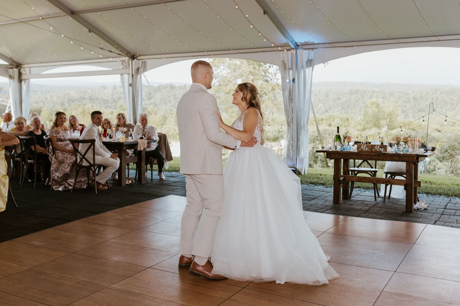 Bride and groom sharing first dance under tent with guests seated and scenic views behind.