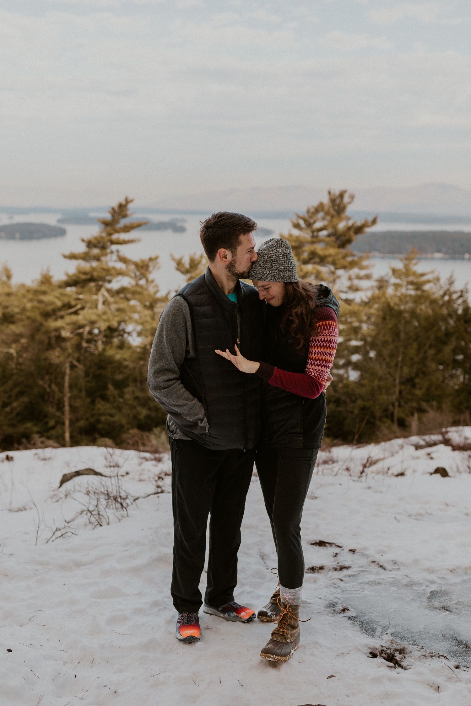 Kirsten admiring her ring while Ivan kisses her forehead in Gilford New Hampshire on Lockes Hill Trail.