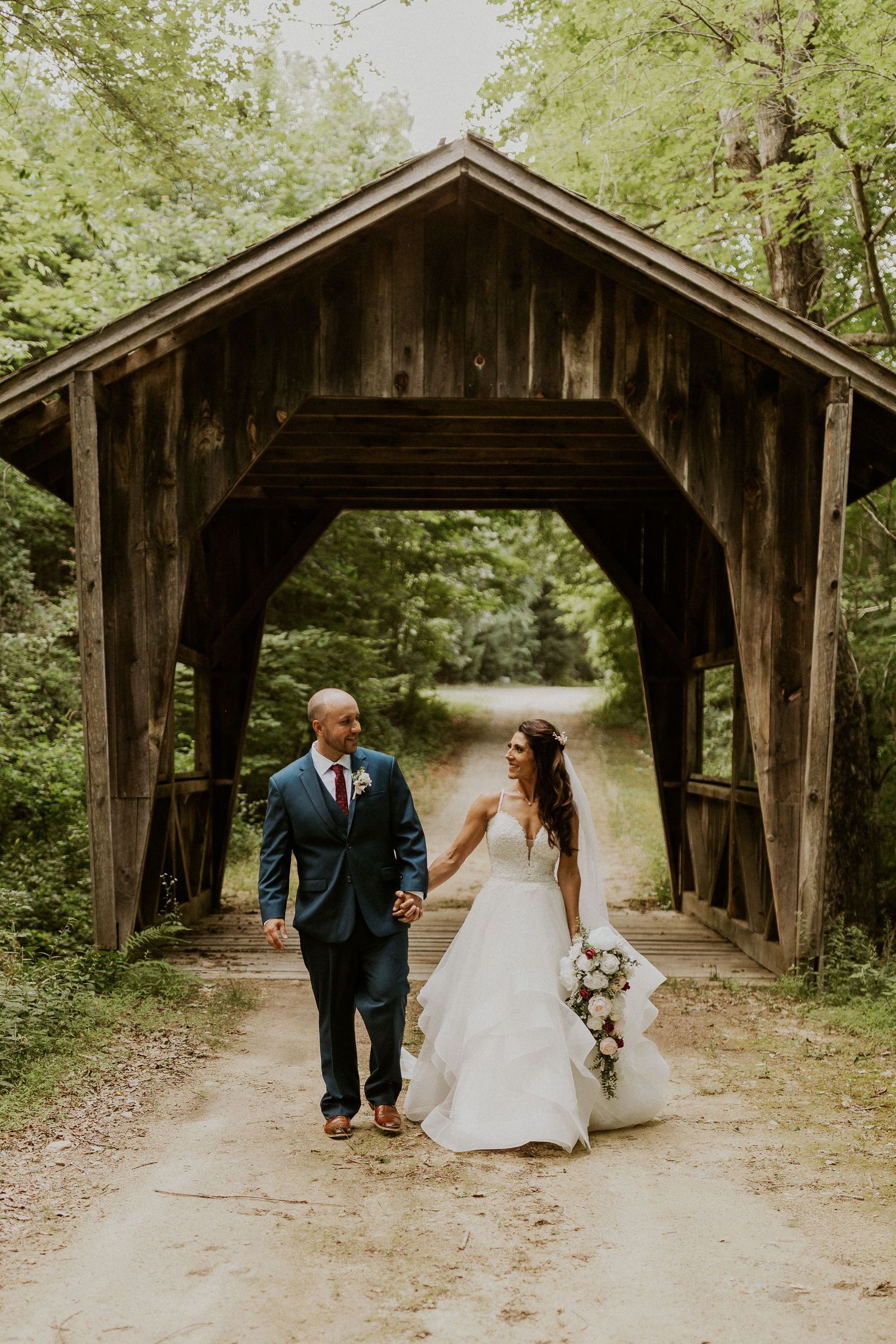 Wedding couple poses for photos under a rustic wooden covered bridge.