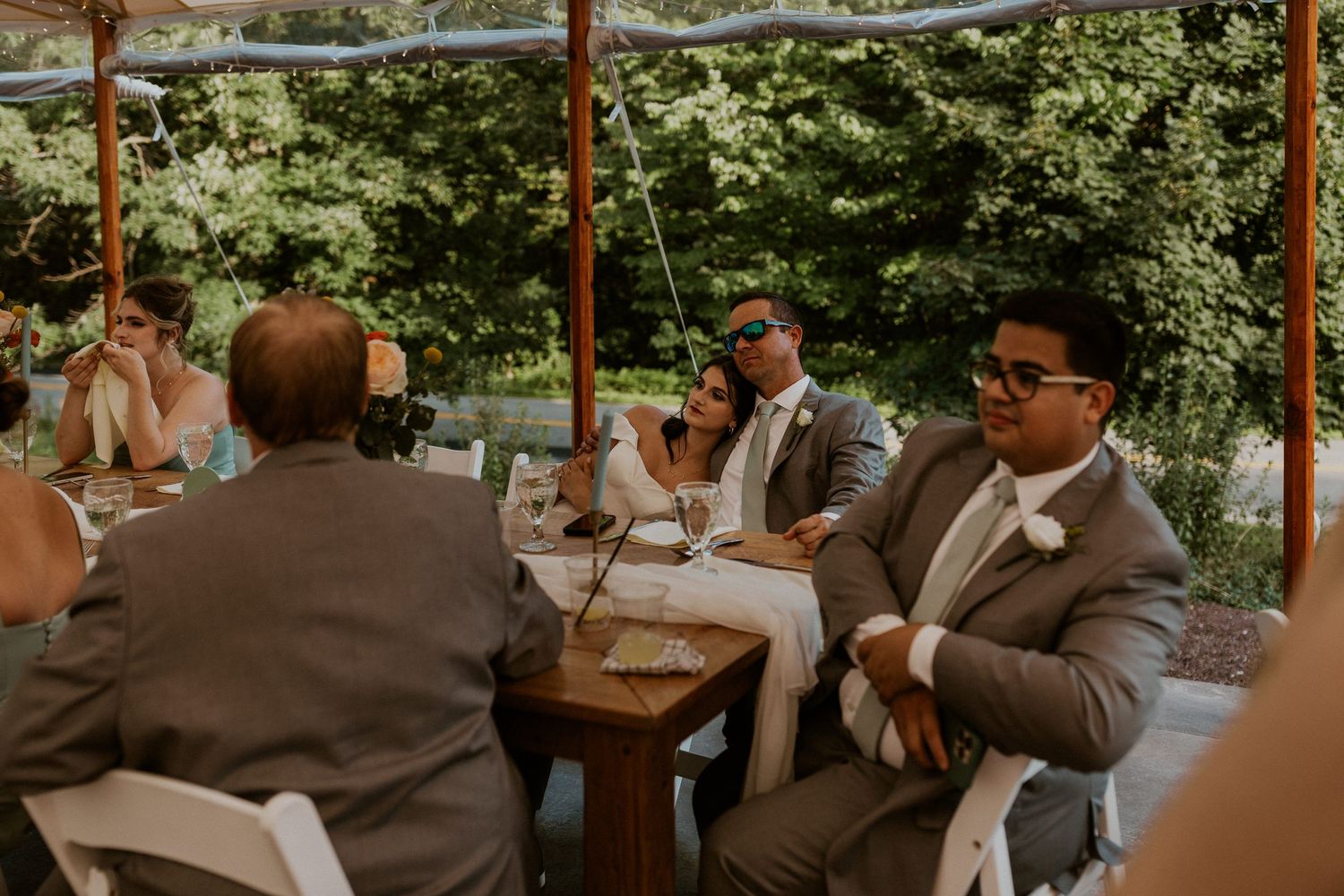 Wedding reception guests enjoying themselves under a tent with natural lighting.