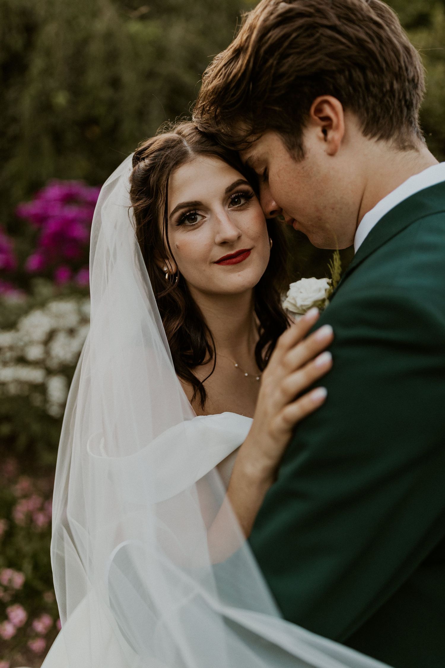 An intimate wedding portrait captured in front of blooming flowers with soft, moody lighting.
