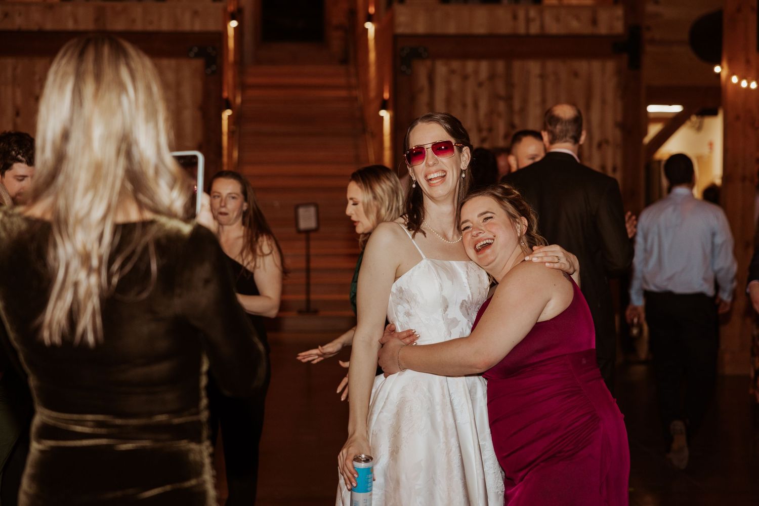 People dancing and celebrating at an indoor wedding reception with warm lighting in a rustic wooden venue.