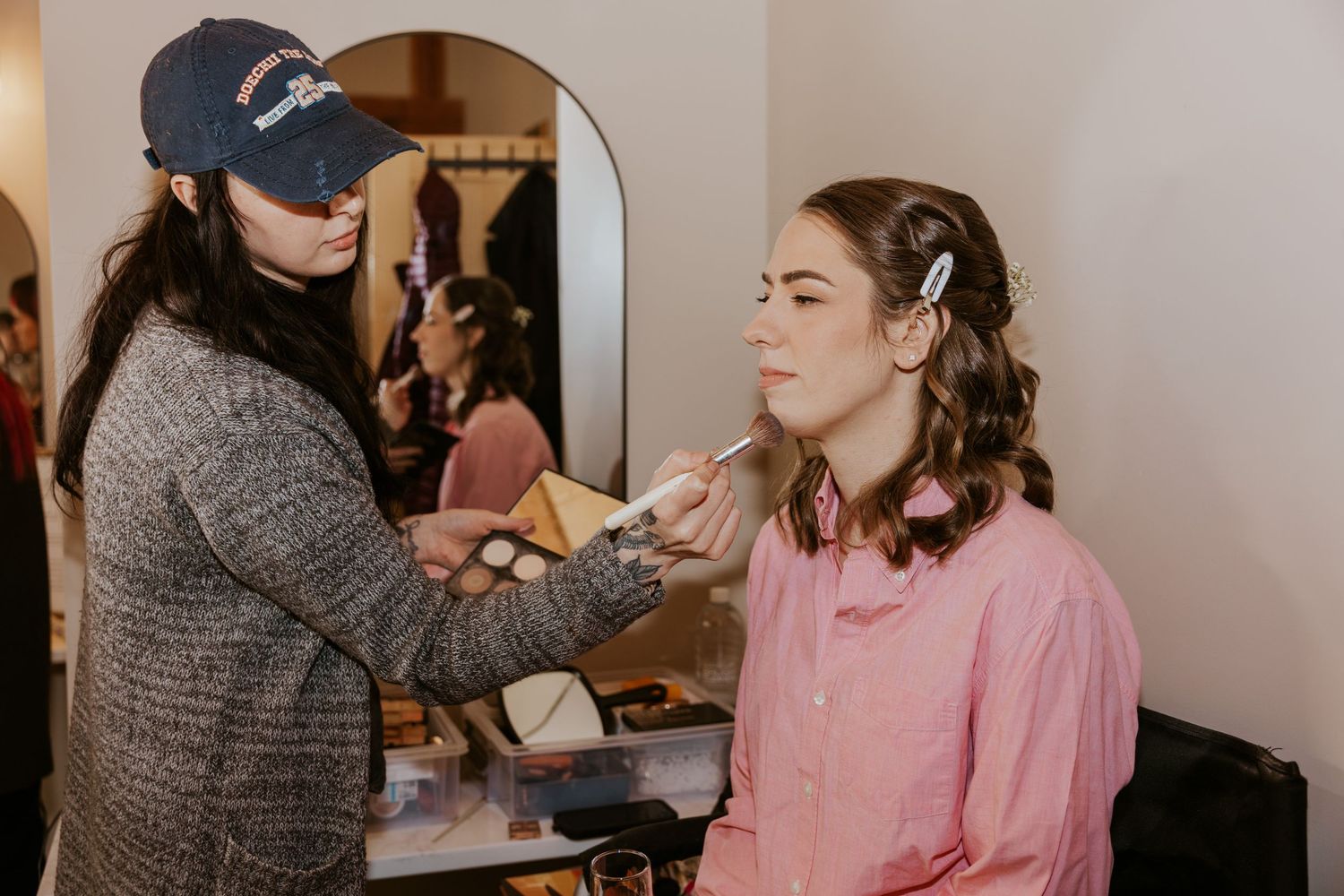 A makeup artist applies cosmetics to a client wearing a pink robe during a professional beauty session.