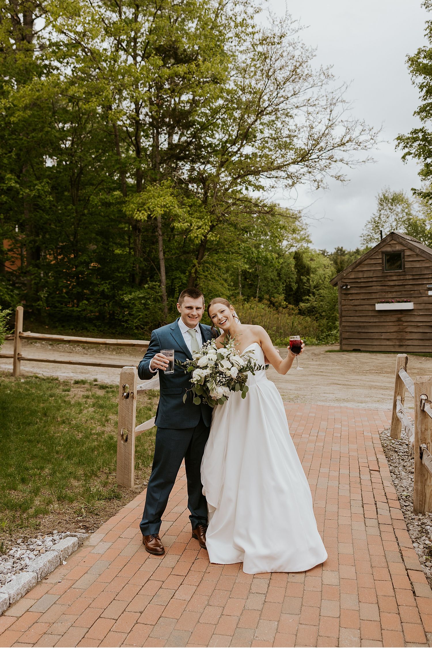 Newlyweds walking and celebrating on a brick pathway surrounded by greenery.