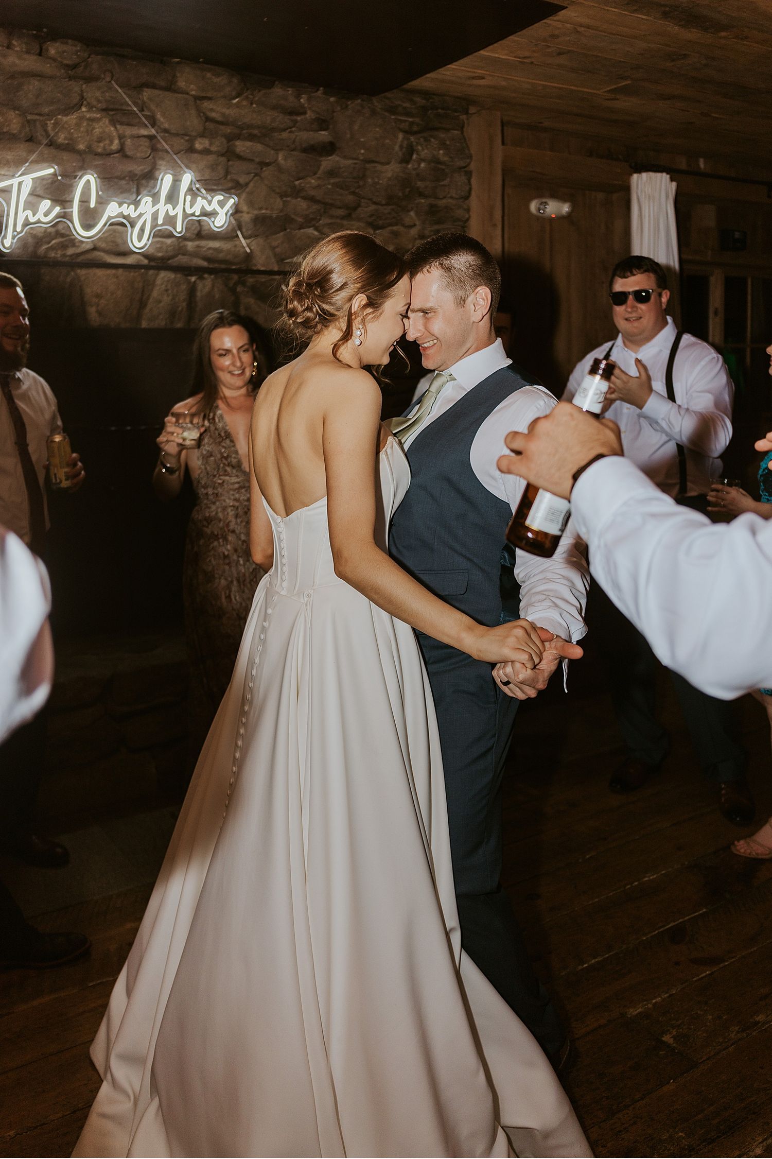 Wedding reception dance floor filled with guests celebrating in a dimly lit rustic barn setting.