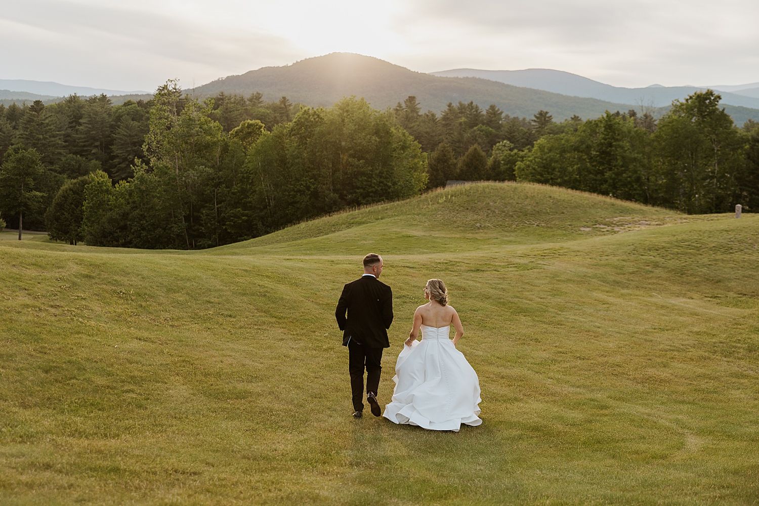 Bride and groom walking across a field at sunset with the mountains in the background at the Owl's Nest in NH