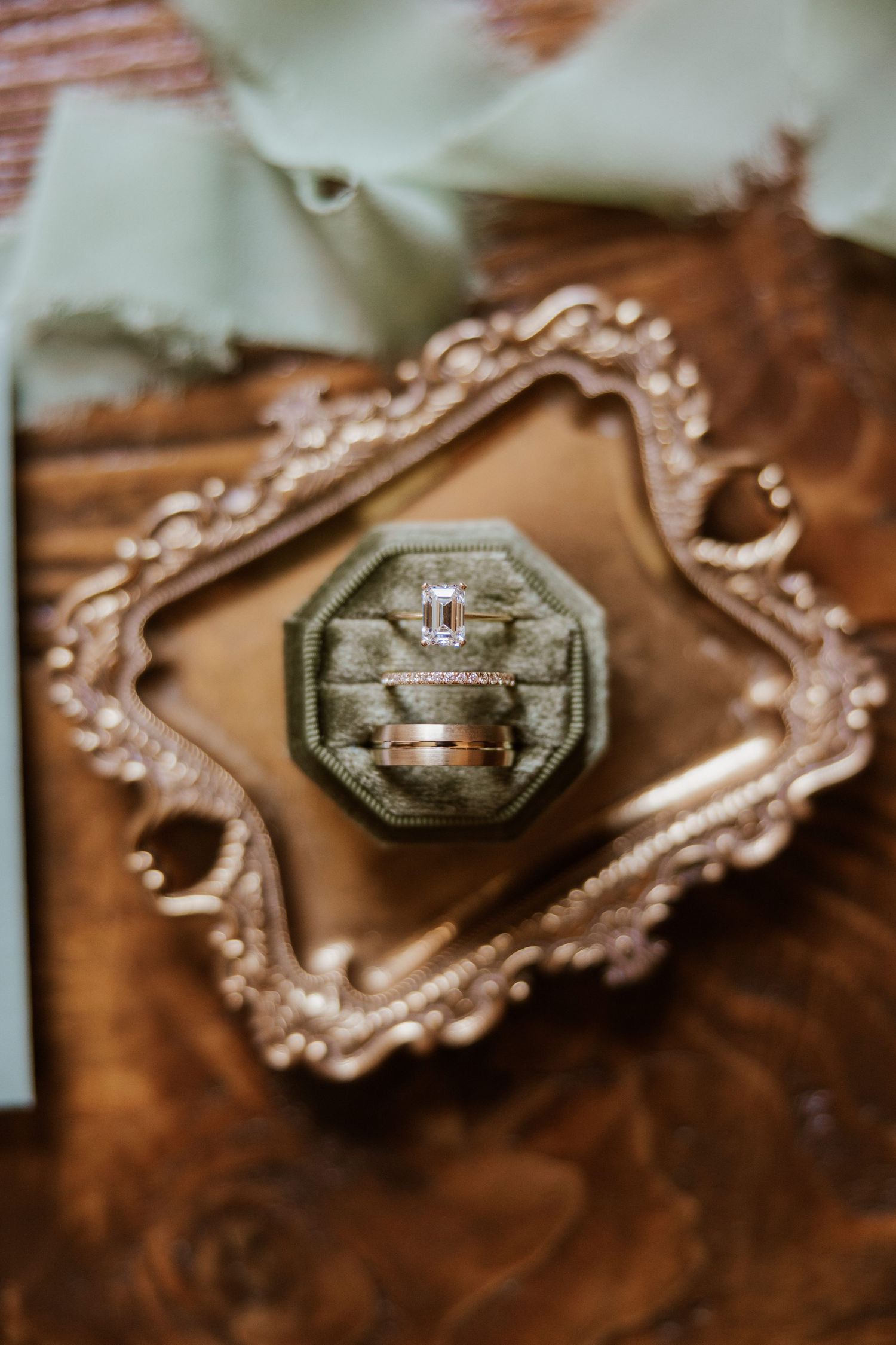Elegant wedding rings displayed in a green velvet octagonal box on an ornate gold tray.