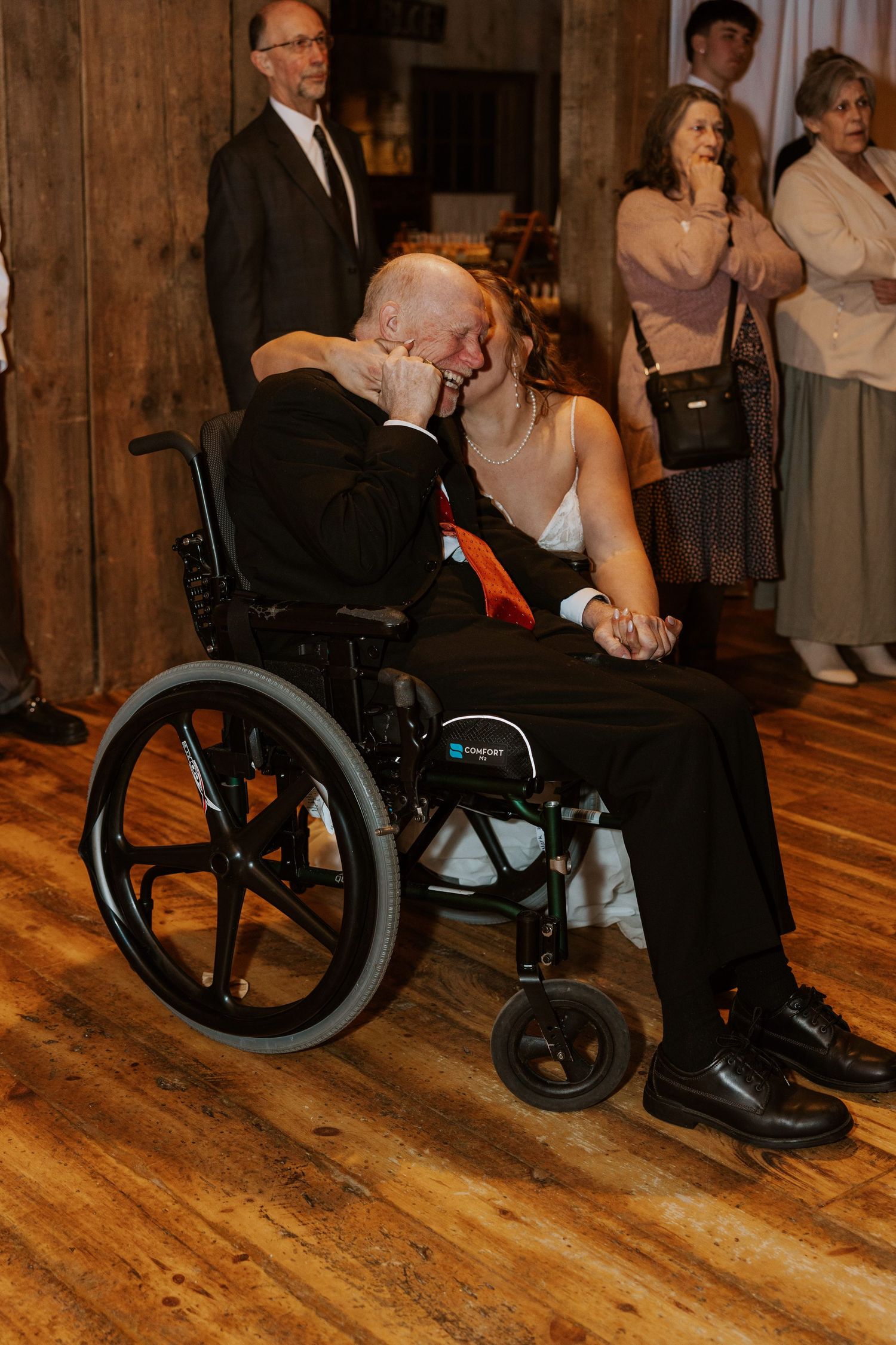 An emotional wedding moment shared with a guest in a wheelchair on hardwood floors.