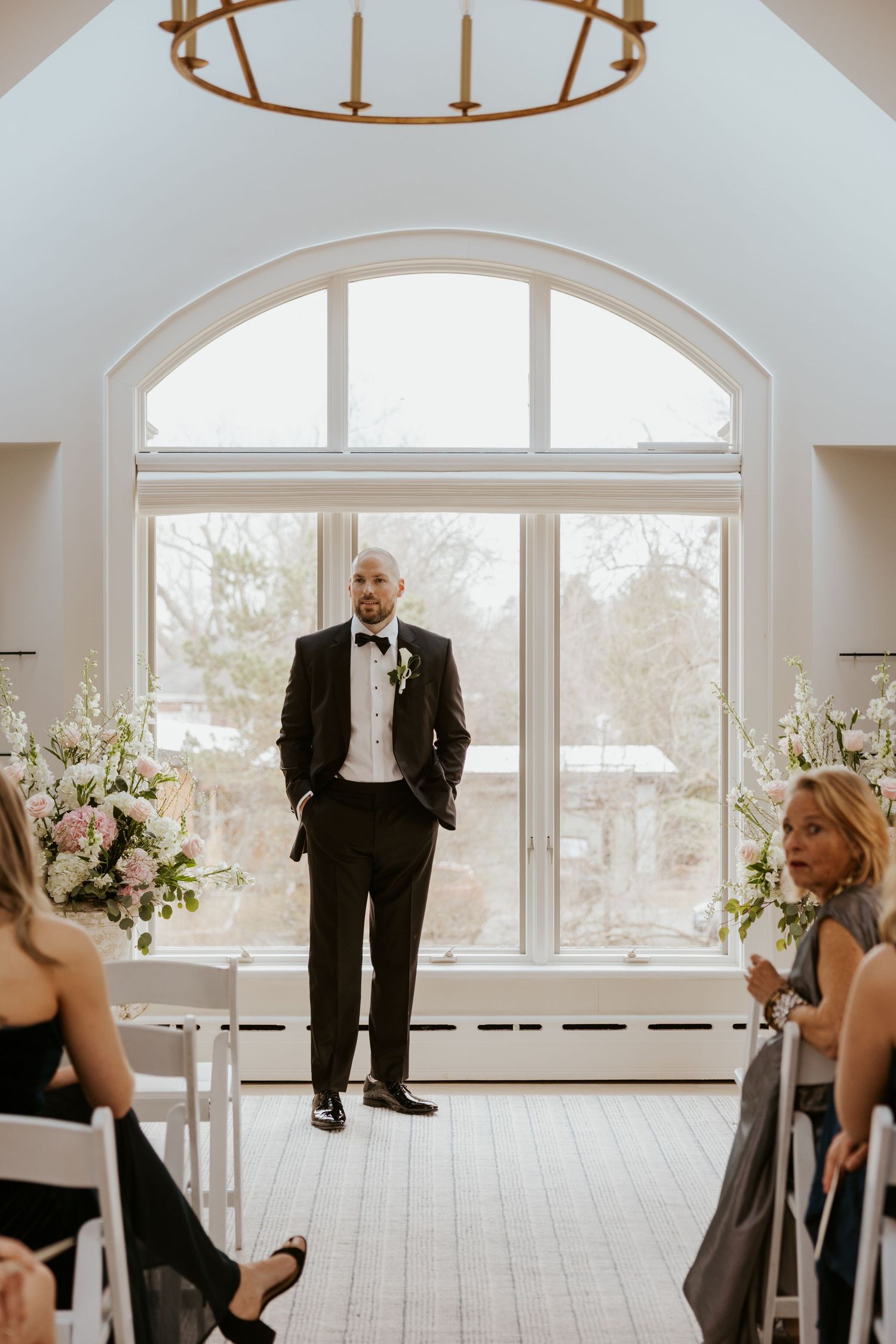 Wedding venue interior with large arched windows and elegant white floral arrangements on dining tables.